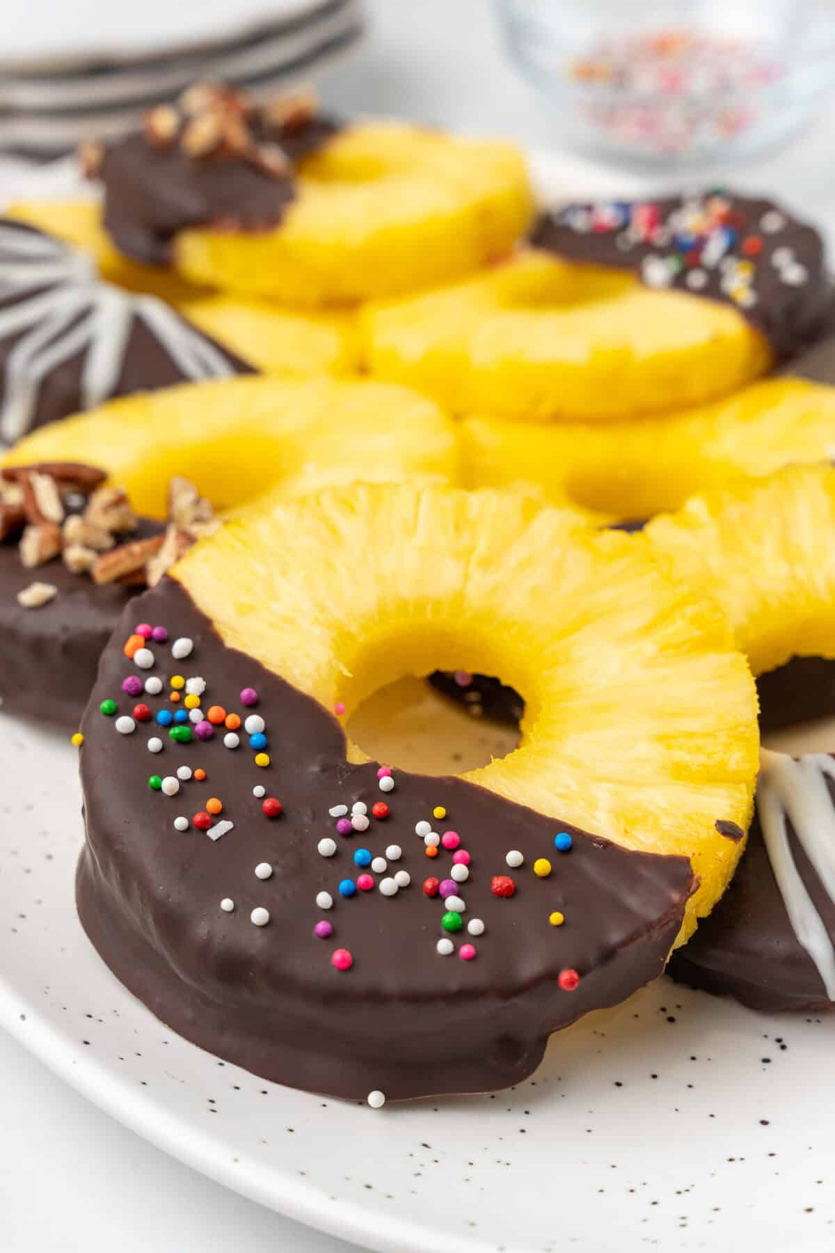 Chocolate covered pineapple with sprinkles on a white platter. 