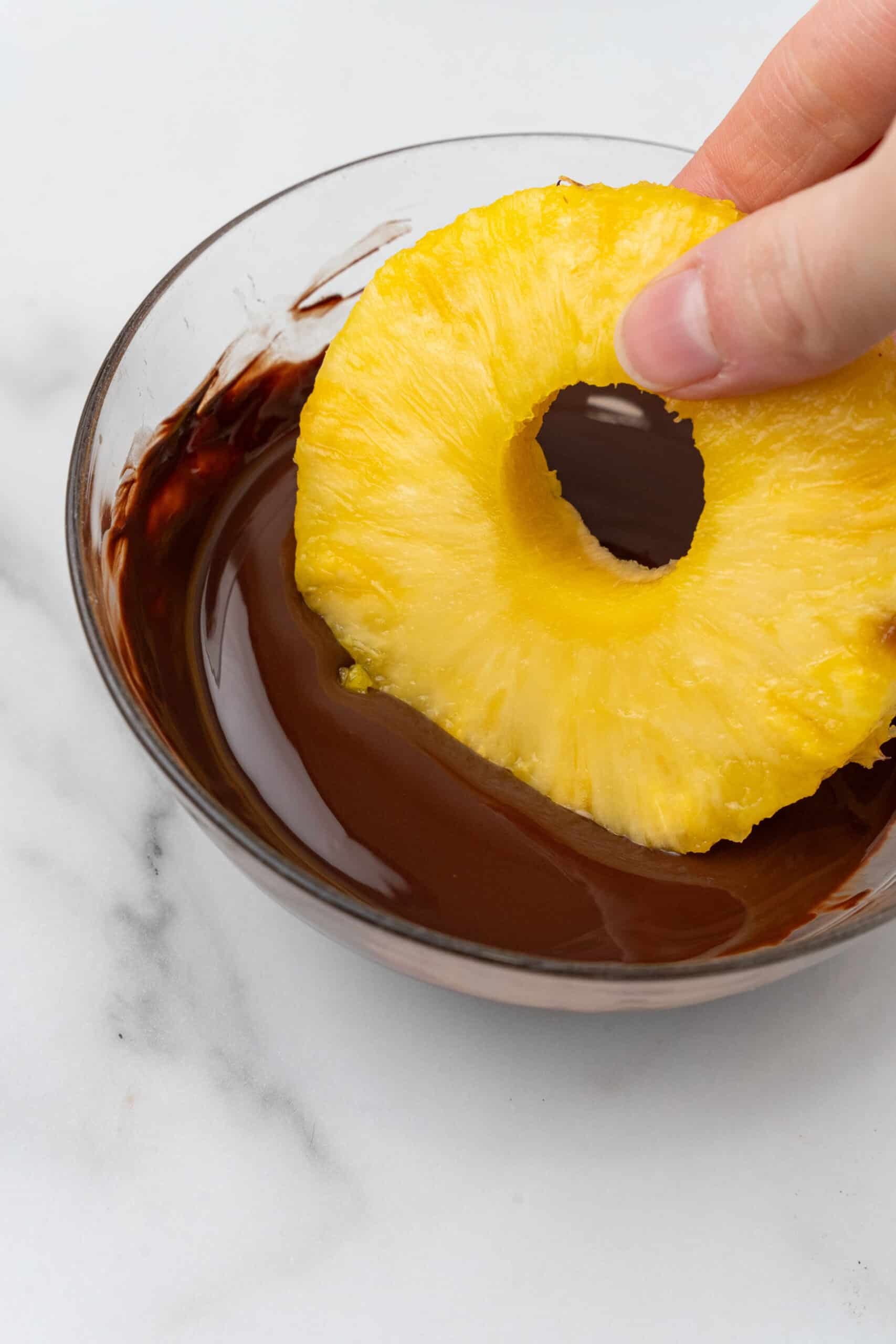 Pineapple being dipped in melted chocolate. 