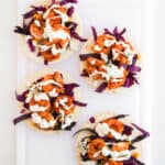 Four mouthwatering shrimp tacos with grilled shrimp, purple cabbage, and corn, all drizzled with a tangy cilantro lime crema, beautifully arranged on a white cutting board. These are the perfect seafood recipe for taco night!.