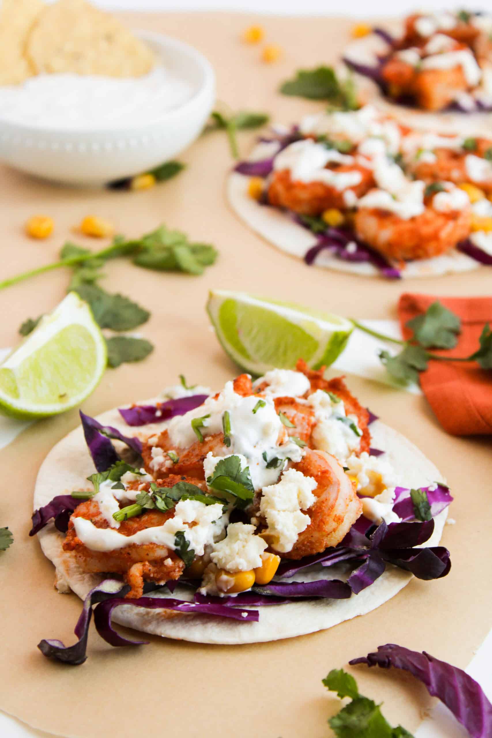 Savor the vibrant flavors of shrimp tacos with cabbage, corn, and cheese, drizzled with cilantro lime crema. Garnished with fresh cilantro and lime wedges, these tasty delights are served on parchment paper for a delightful meal you won't forget.