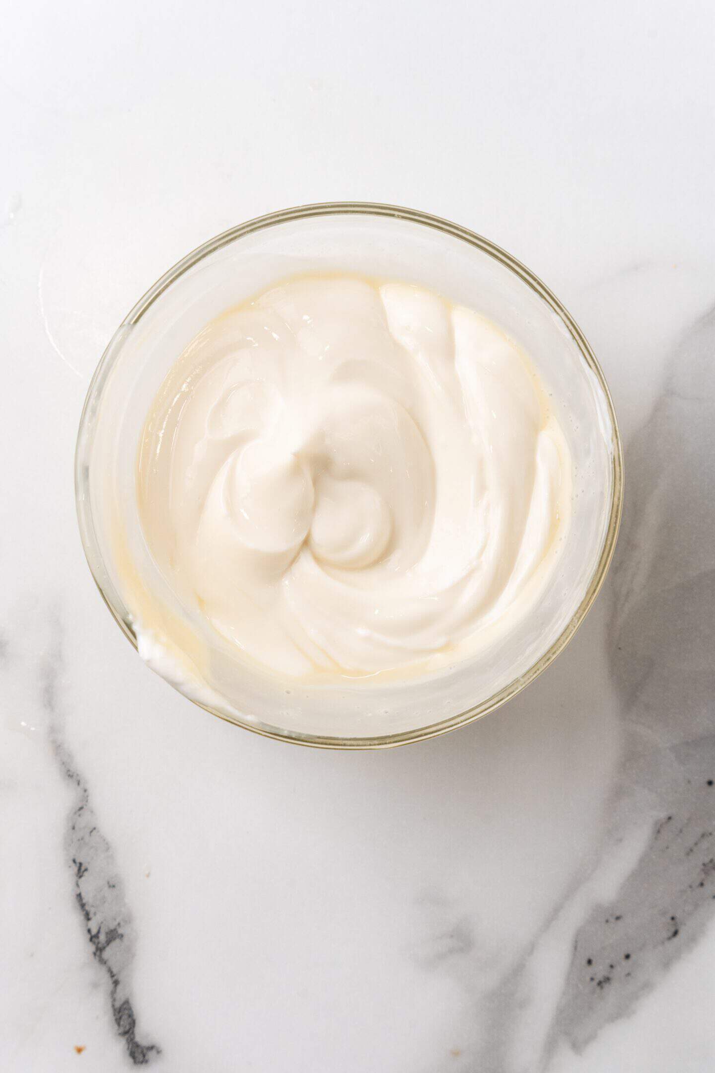 A clear glass bowl filled with creamy white yogurt and a swirl of blueberry compote rests on a marble surface, evoking the essence of a luscious cheesecake.