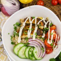 Savor the vibrant Chicken Shawarma Bowl featuring grilled chicken, brown rice, cucumber, red onion, and cherry tomatoes topped with a drizzle sauce. Complemented by fresh lemon, cherry tomatoes, red onion, and parsley on a woven basket for an enticing touch.