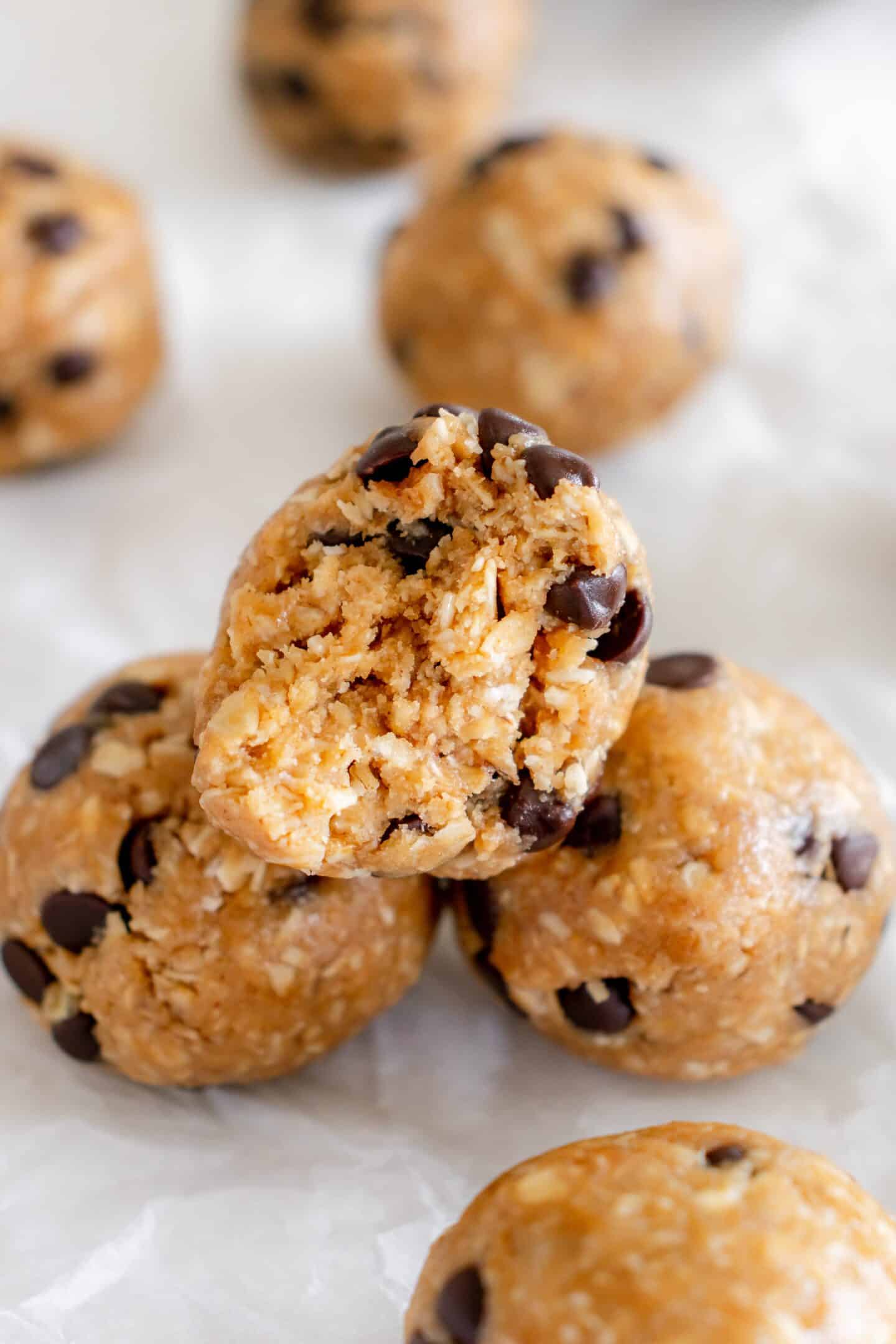 Delight in these no-bake cookie dough protein balls, packed with chocolate chips, beautifully stacked on parchment paper—one with a bite taken out.