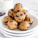 A stack of chocolate chip protein balls on a white plate, resting on a table with a blurred background.