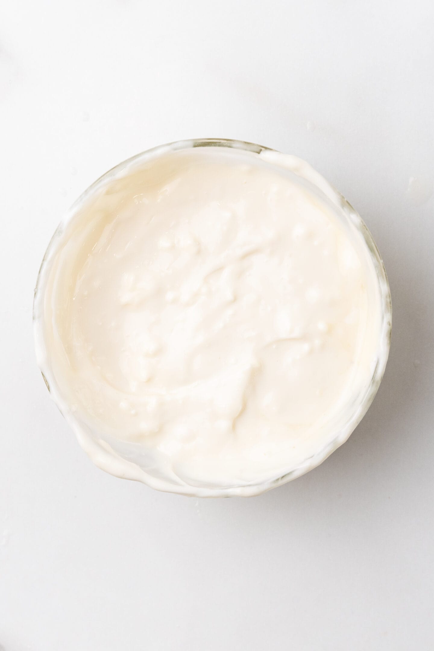 A bowl of creamy white yogurt, reminiscent of lemon cheesecake, sits elegantly on a white surface.