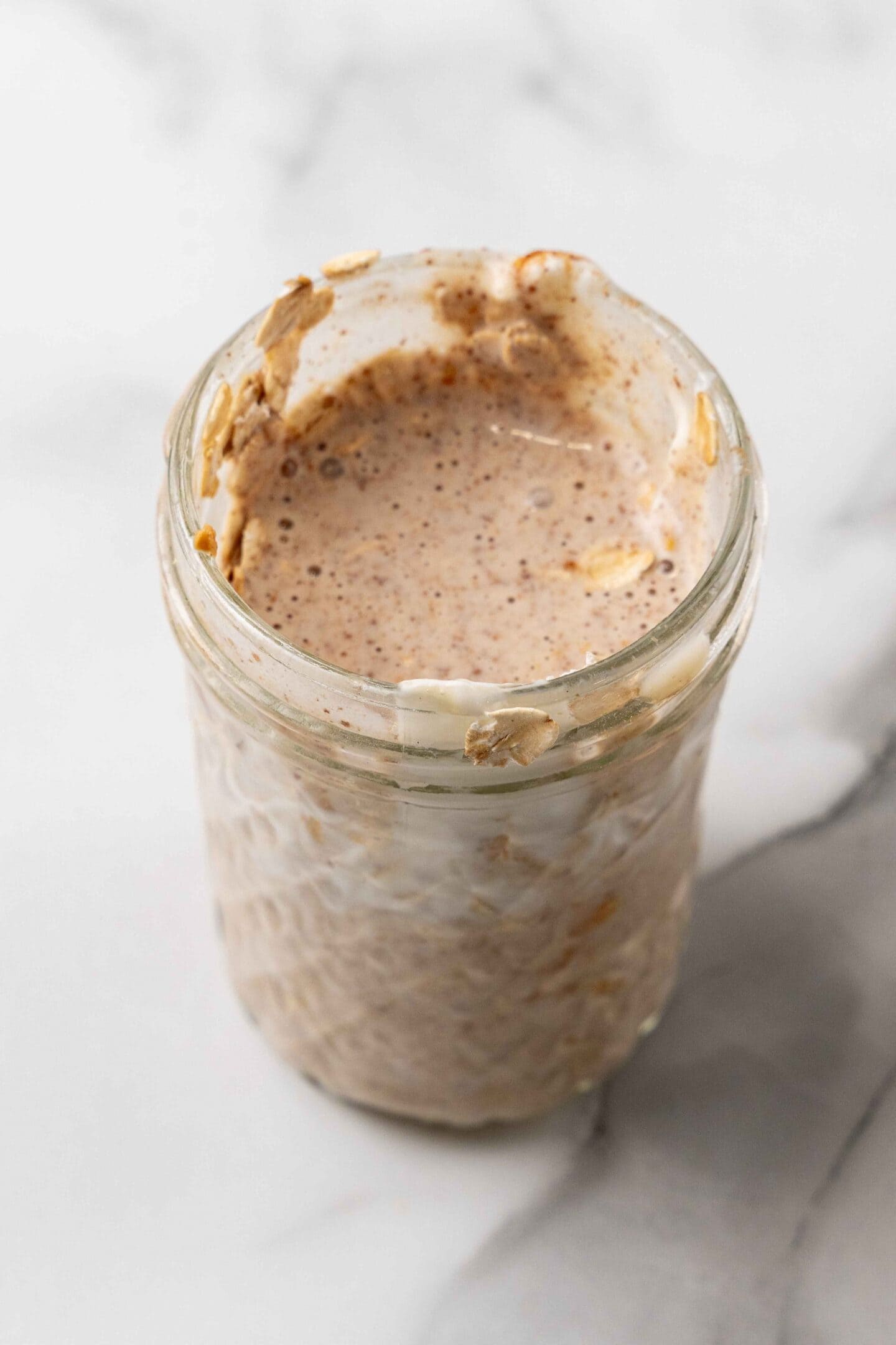 A jar filled with partially eaten overnight oats and almond butter mixture sits on a marble surface, hinting at the presence of chia seeds for an added nutritional boost.