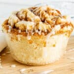 A large cinnamon roll with icing drizzle sits enticingly on a wooden board, offering the indulgent delight of a Single Serve Protein twist.