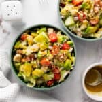 Two bowls of chicken chopped salad with lettuce, avocado, cherry tomatoes, and succulent chicken sit on a marble surface. They are accompanied by a small bowl of honey mustard dressing, forks, and salt and pepper shakers for the perfect salad recipe.