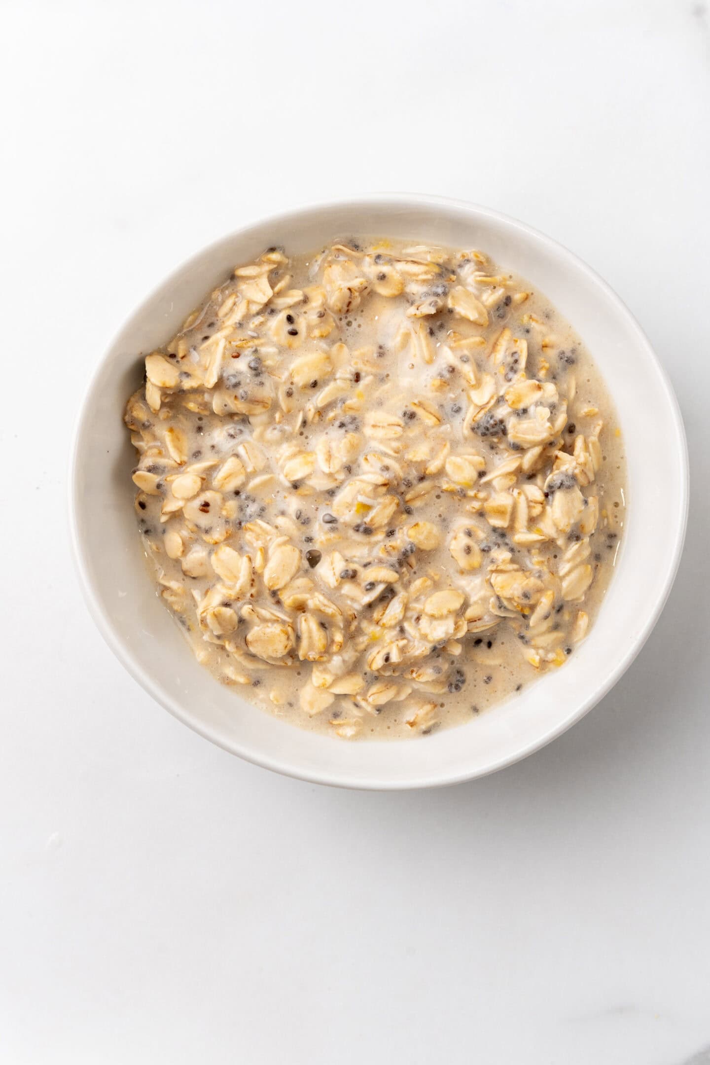 A bowl of creamy overnight oats mixed with milk, chia seeds, and oats sits on a white background, offering a hint of lemon cheesecake flavor.