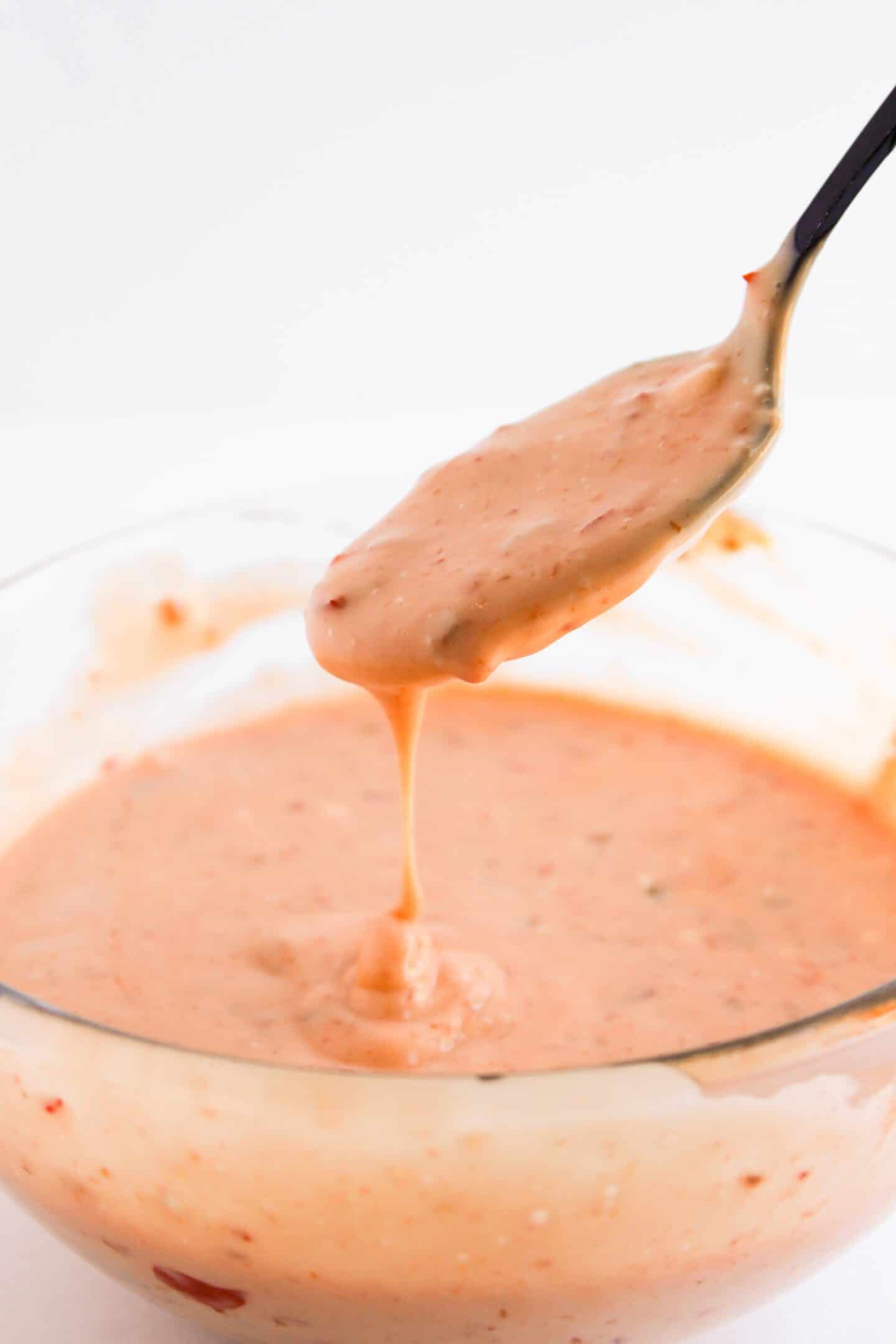 A spoon lifting creamy, orange-colored sauce with visible spices from a glass bowl hints at the rich flavors of Asian cuisine.