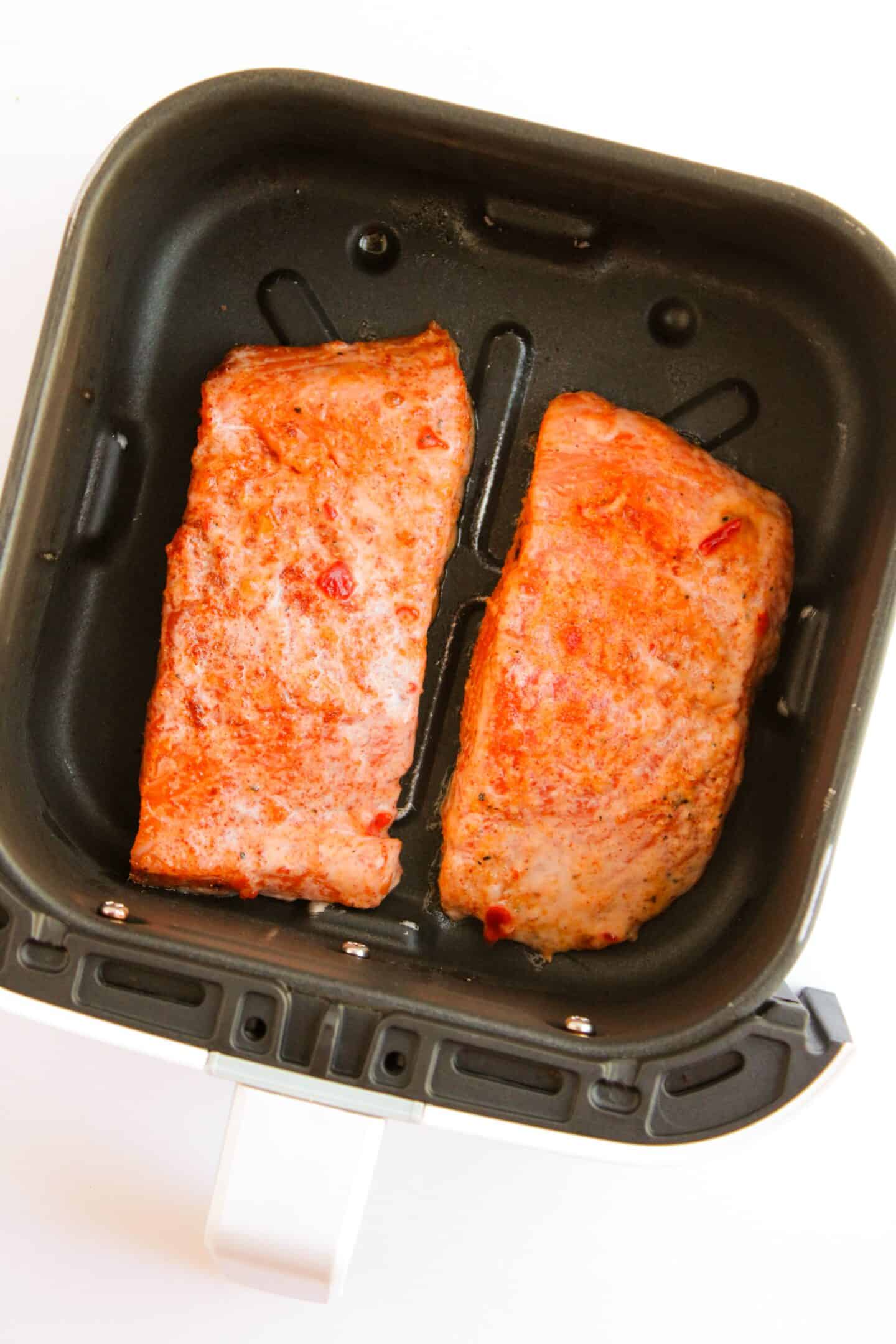 Two seasoned pieces of salmon are cooking in an air fryer basket, creating a simple yet delicious Bang Bang Salmon recipe.