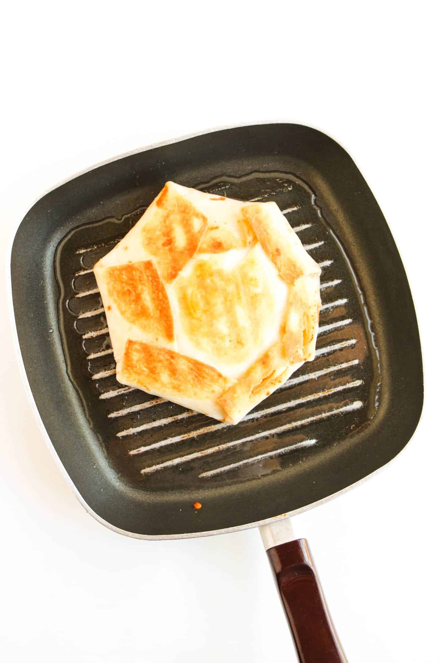A Crunchwrap is being grilled in a square pan with ridges, achieving the perfect sear.