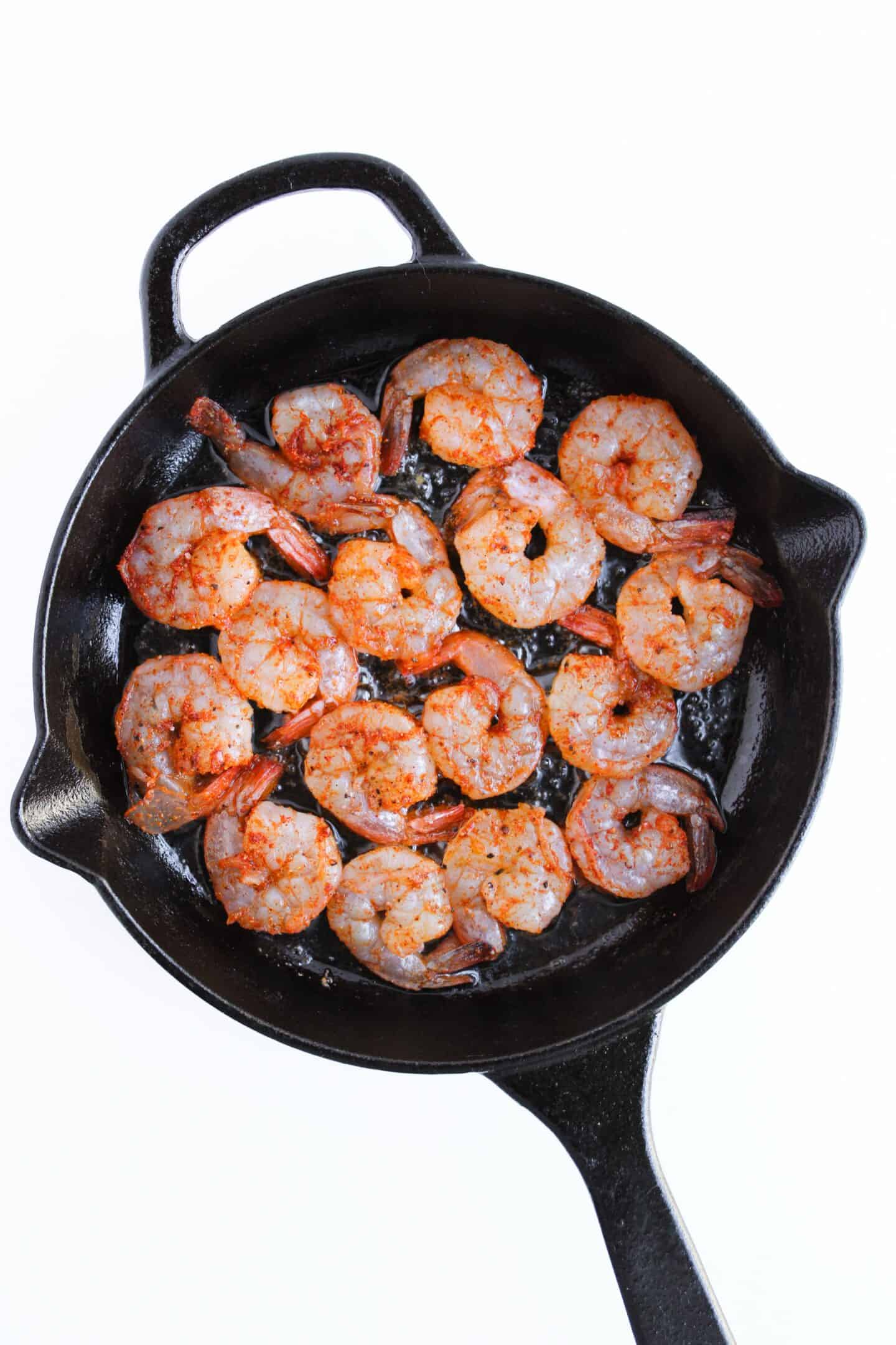 Succulent shrimp sizzle in a black cast-iron skillet, perfectly paired with vibrant chimichurri, all set against a pristine white background. A delightful recipe to elevate your culinary repertoire.