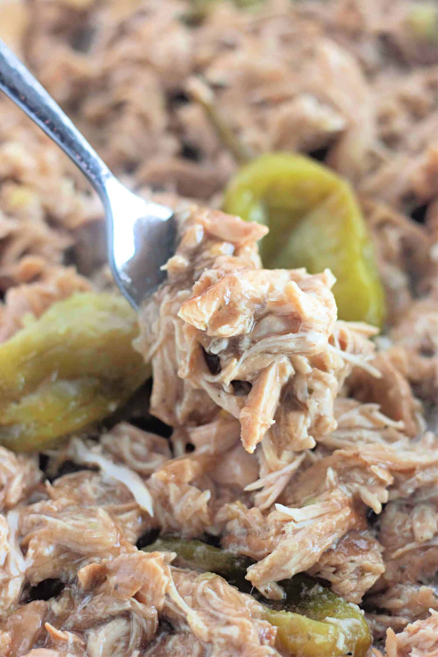 Close-up of flavorful Mississippi-style shredded chicken mixed with vibrant peppers, being scooped by a spoon.