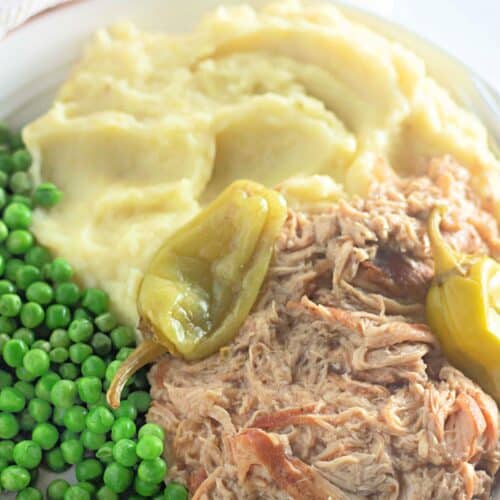 Mississippi Chicken shredded in rich gravy, served with creamy mashed potatoes and green peas, all garnished with vibrant peppers.