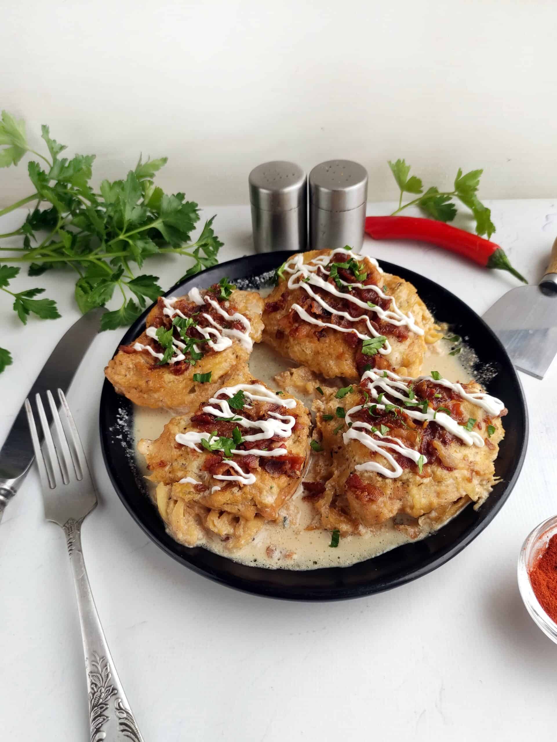 A black plate showcases four fritters topped with a creamy ranch sauce, garnished with fresh green herbs. A silver knife and fork rest elegantly beside them, while salt and pepper shakers stand ready in the background.
