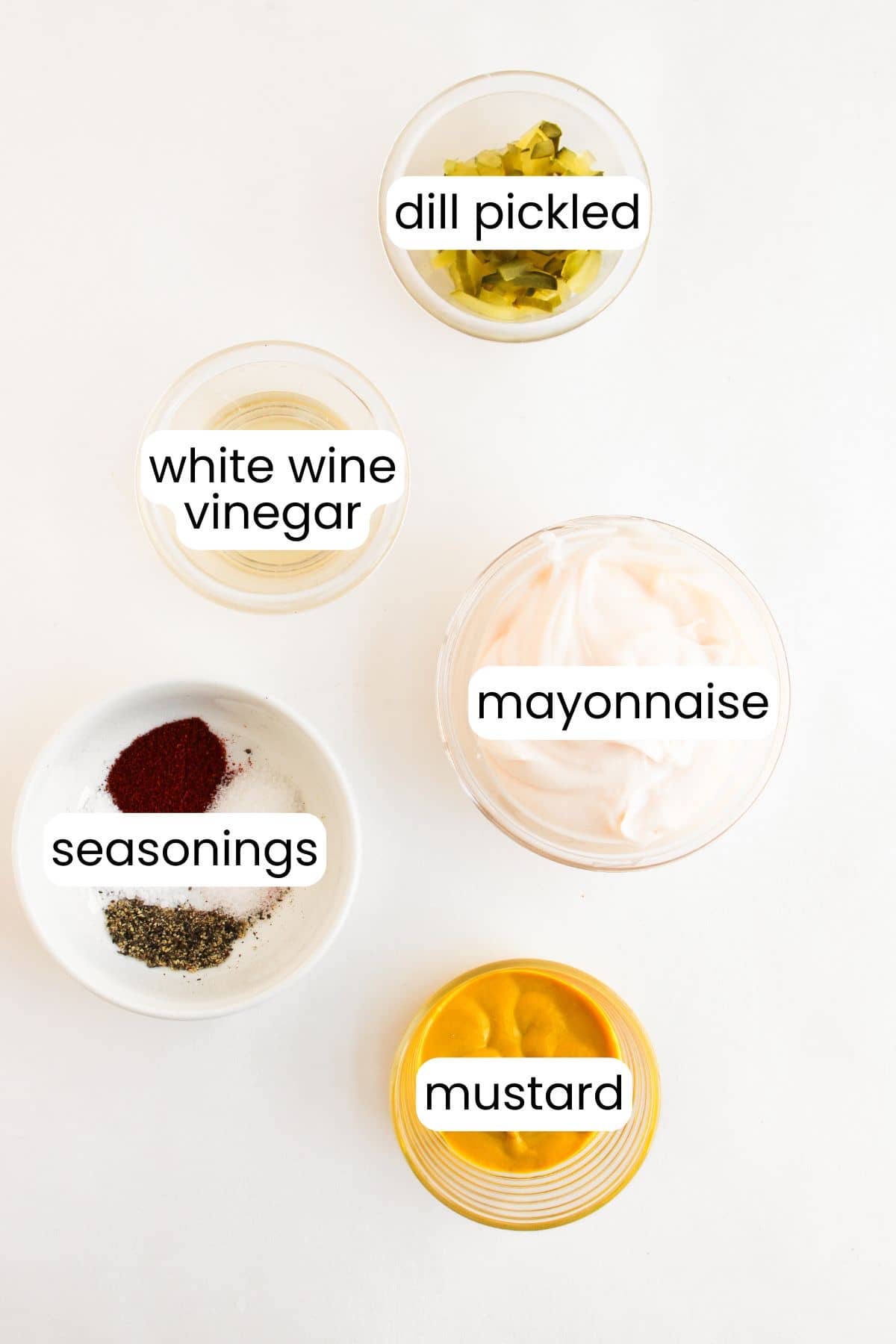 Containers with ingredients like dill pickles, white wine vinegar, mayonnaise, and seasonings such as paprika and black pepper evoke the irresistible tang of a Big Mac. Mustard completes this harmonious blend against a light background.