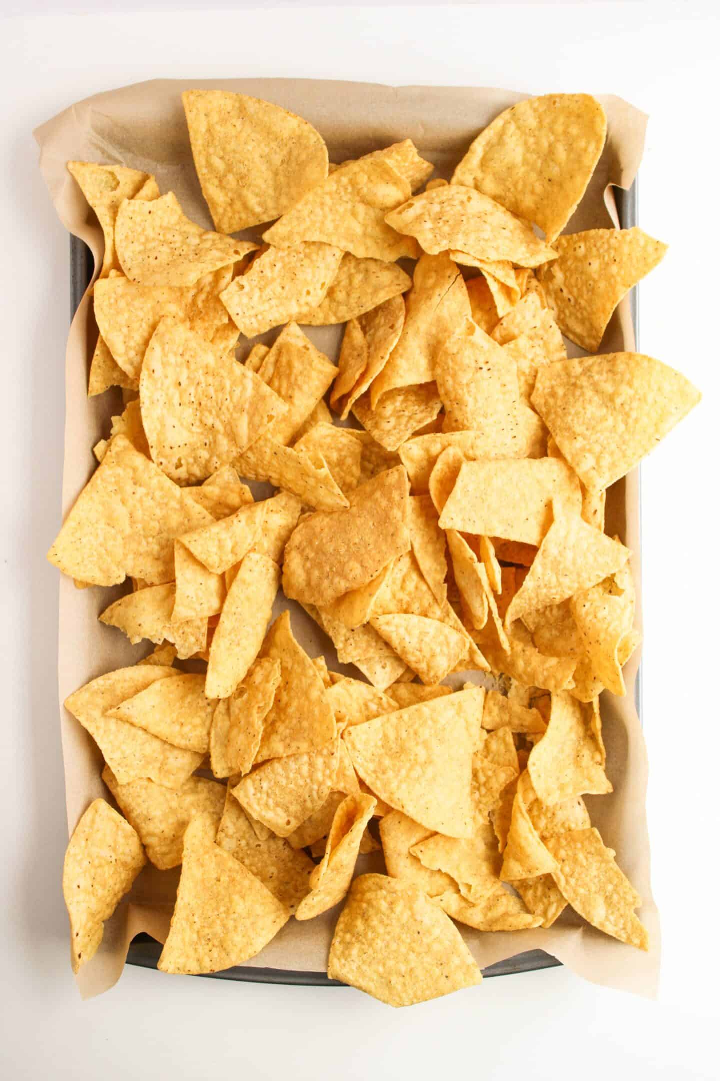 A sheet pan brimming with yellow tortilla chips rests on parchment paper, ready to become delicious nachos.