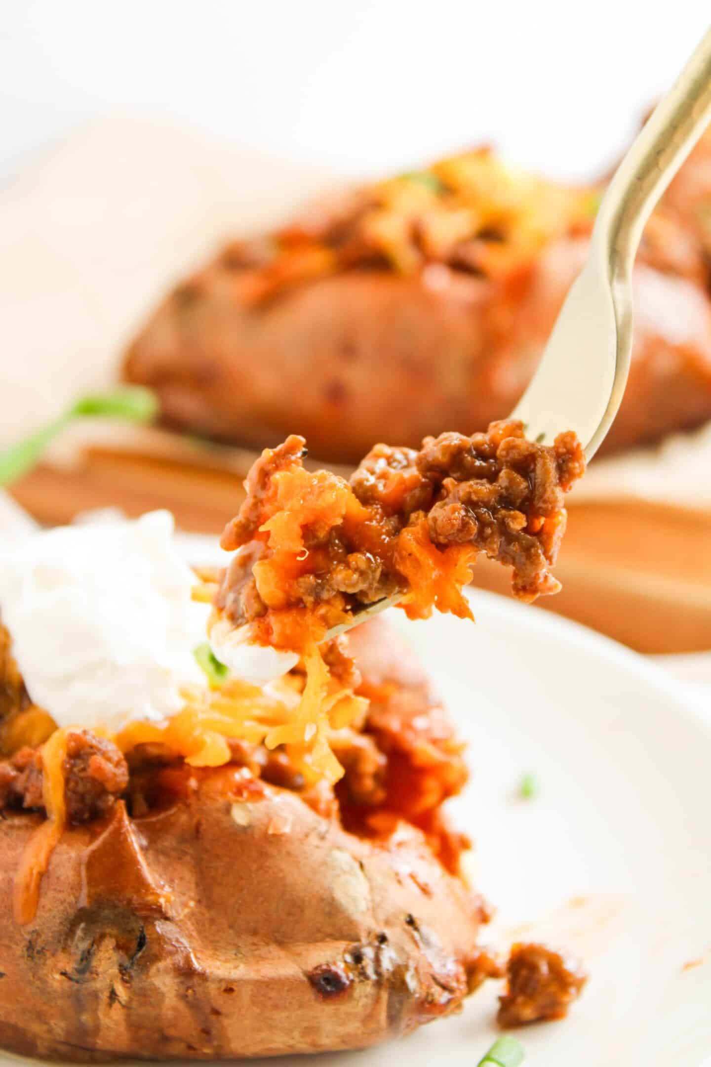 A fork holds a tempting bite of loaded baked sweet potato topped with ground beef, melted cheese, and luscious sour cream—like a twist on classic Sloppy Joes.