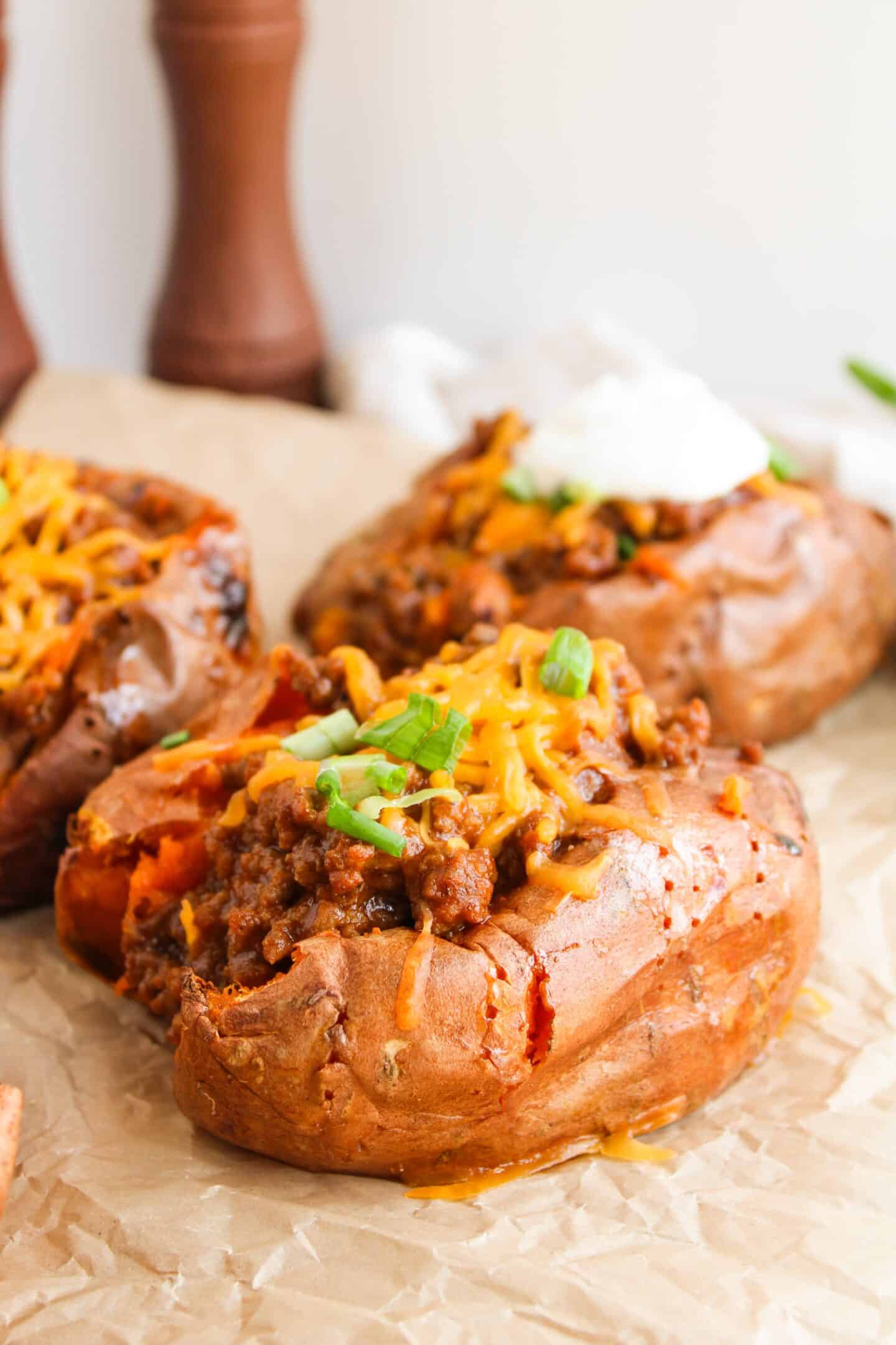Baked sweet potatoes topped with savory Sloppy Joes, melted cheese, and chopped green onions on parchment paper.