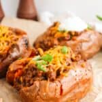 Baked sweet potatoes topped with savory Sloppy Joes, melted cheese, and chopped green onions on parchment paper.
