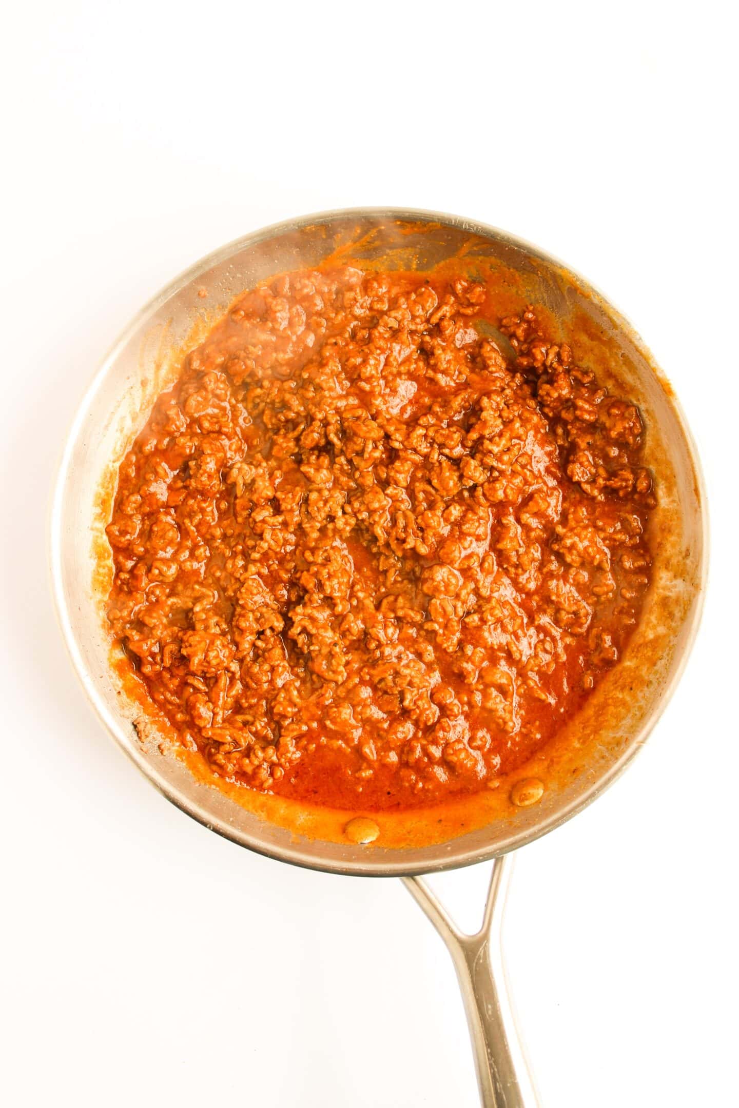 Ground beef cooking in a skillet with a red sauce, reminiscent of classic Sloppy Joes, viewed from above on a white background.