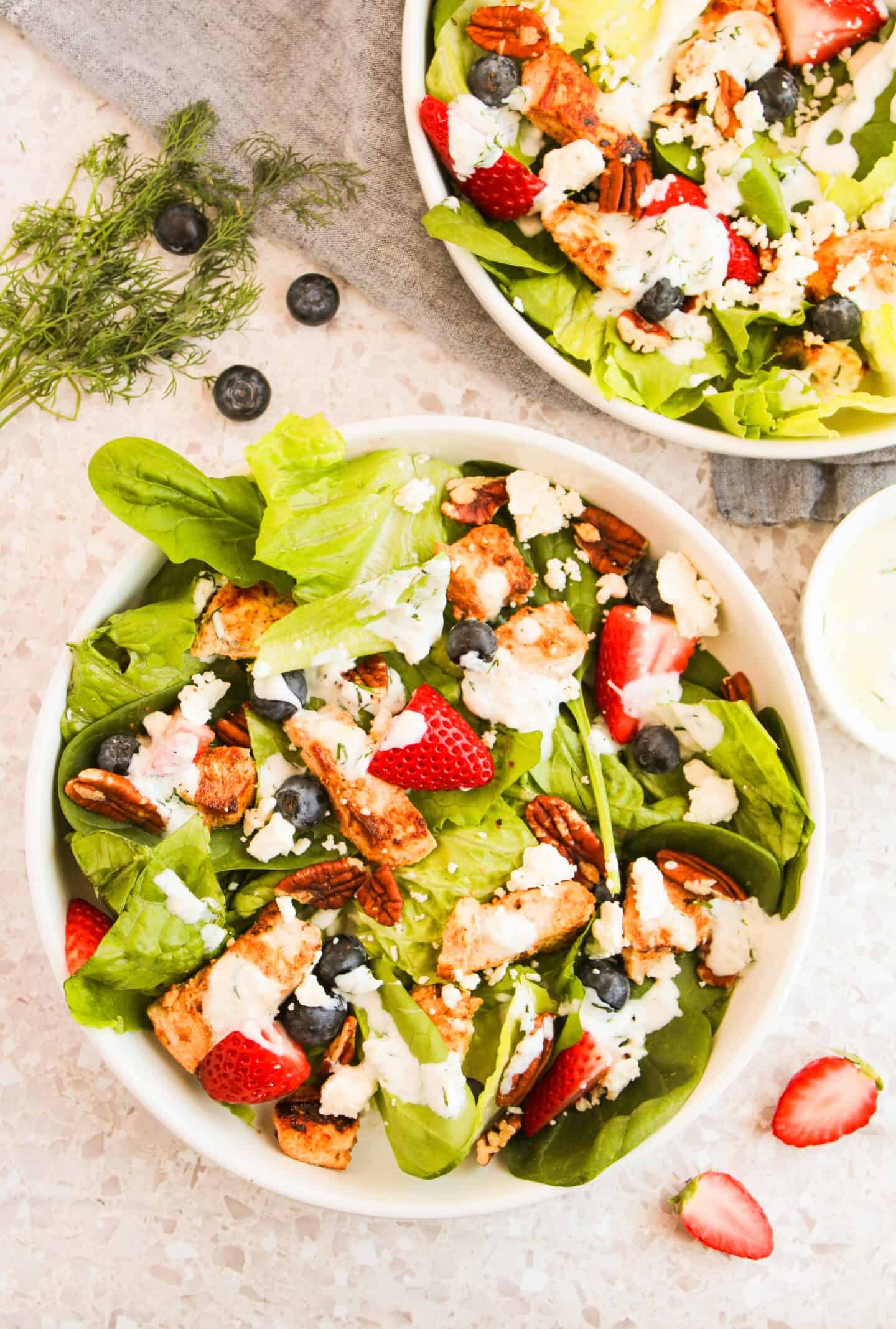 Savor a chicken salad featuring lettuce, strawberries, blueberries, and pecans, topped with grilled chicken and crumbled cheese. It's all drizzled with a creamy dressing made from Greek yogurt for a delightful twist.
