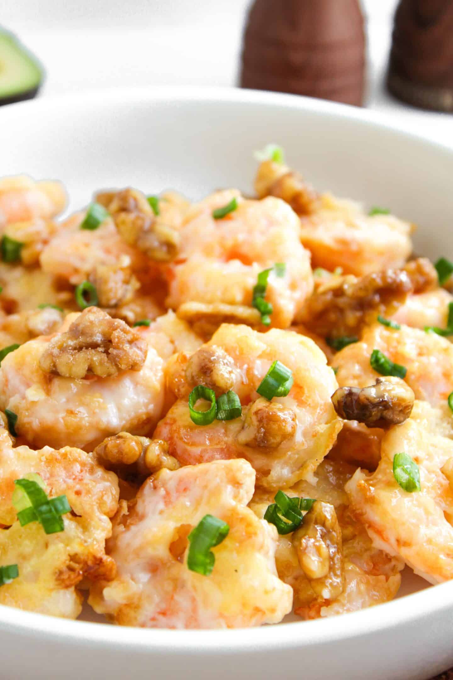A bowl of Honey Walnut Shrimp topped with green onions, featuring perfectly sautéed shrimp and crunchy walnuts for a delightful twist.