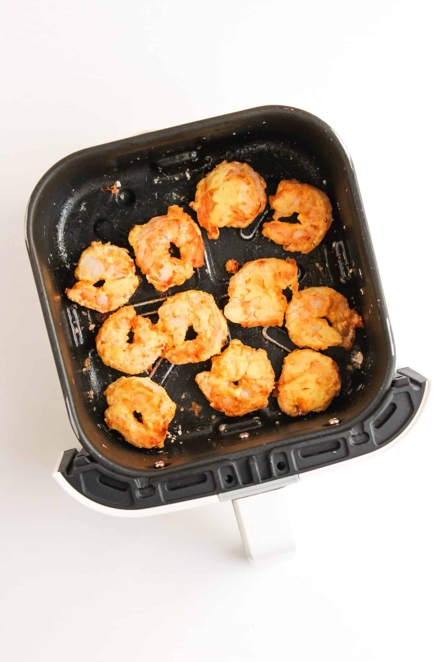 An air fryer basket holds ten perfectly cooked breaded onion rings.