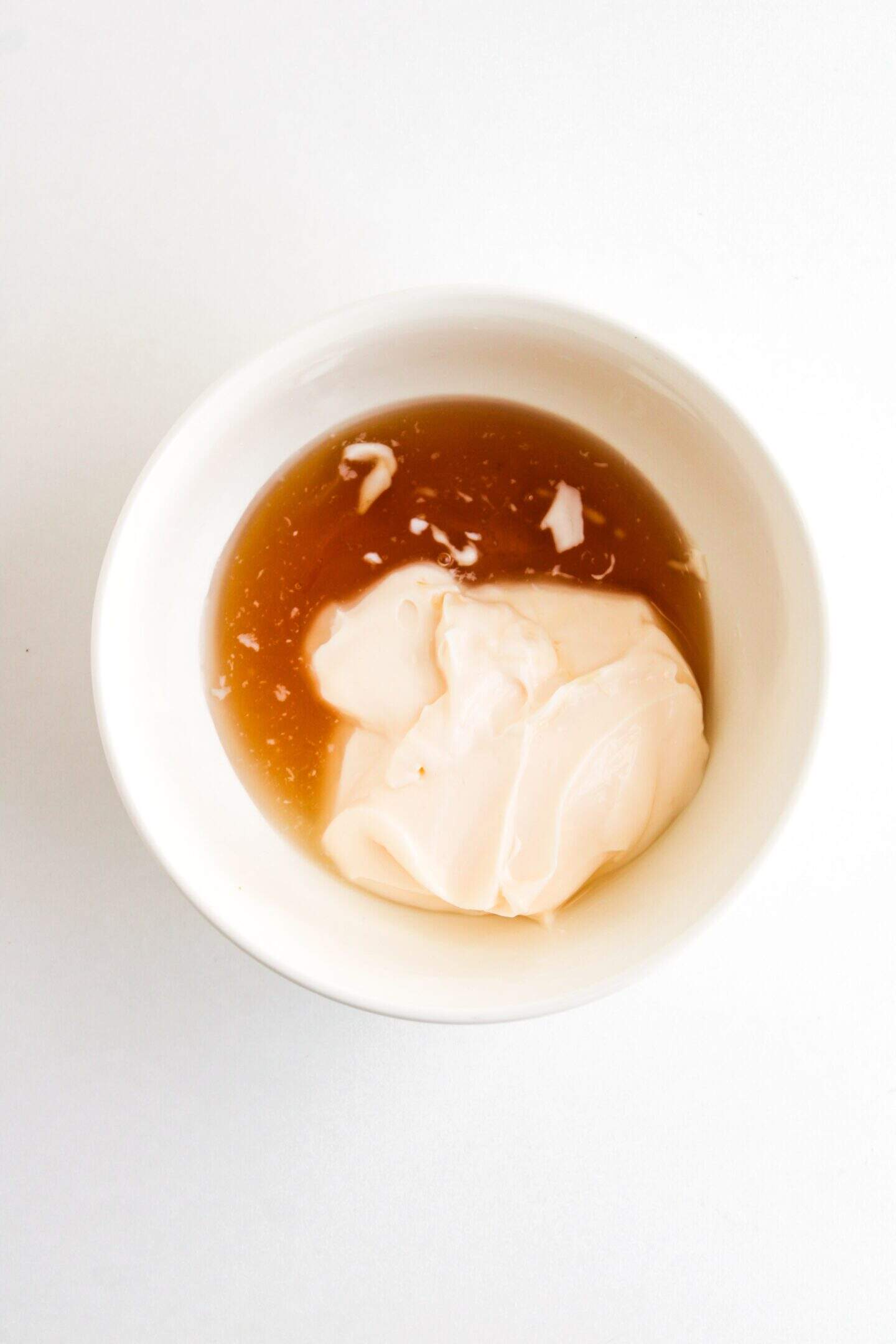 A bowl featuring a dollop of mayonnaise and brown sauce sits on a pristine white backdrop, reminiscent of the creamy textures found in Honey Walnut Shrimp dishes prepared in an Air Fryer.