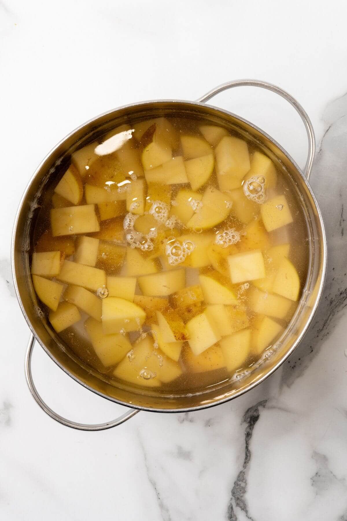 A pot of boiling water with diced potatoes sits on a marble surface, ready to transform into a delectable Big Mac casserole.