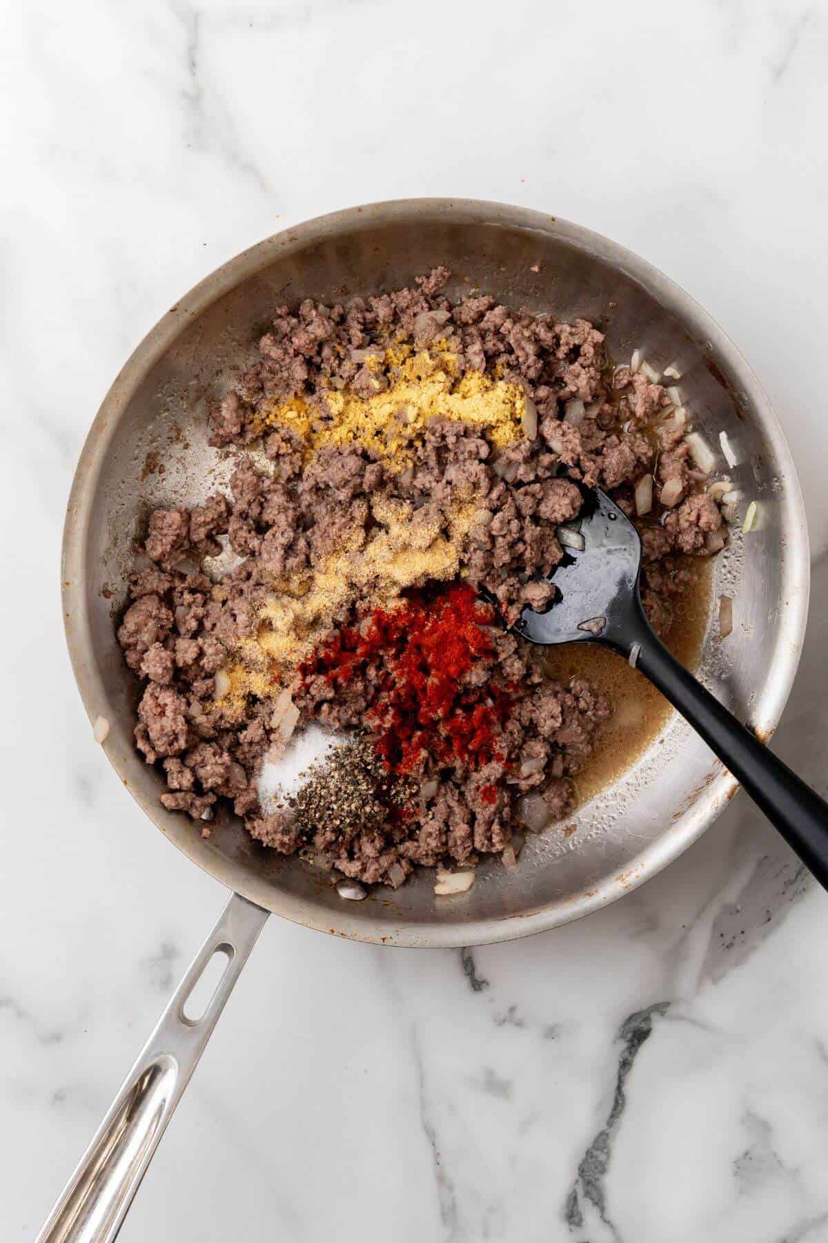 A delicious skillet of ground meat sizzles with spices like paprika and pepper, while a black spatula rests nearby, inviting you to imagine this savory mix as the perfect base for your next Big Mac-inspired casserole. The smell alone promises a recipe full of bold flavors.
