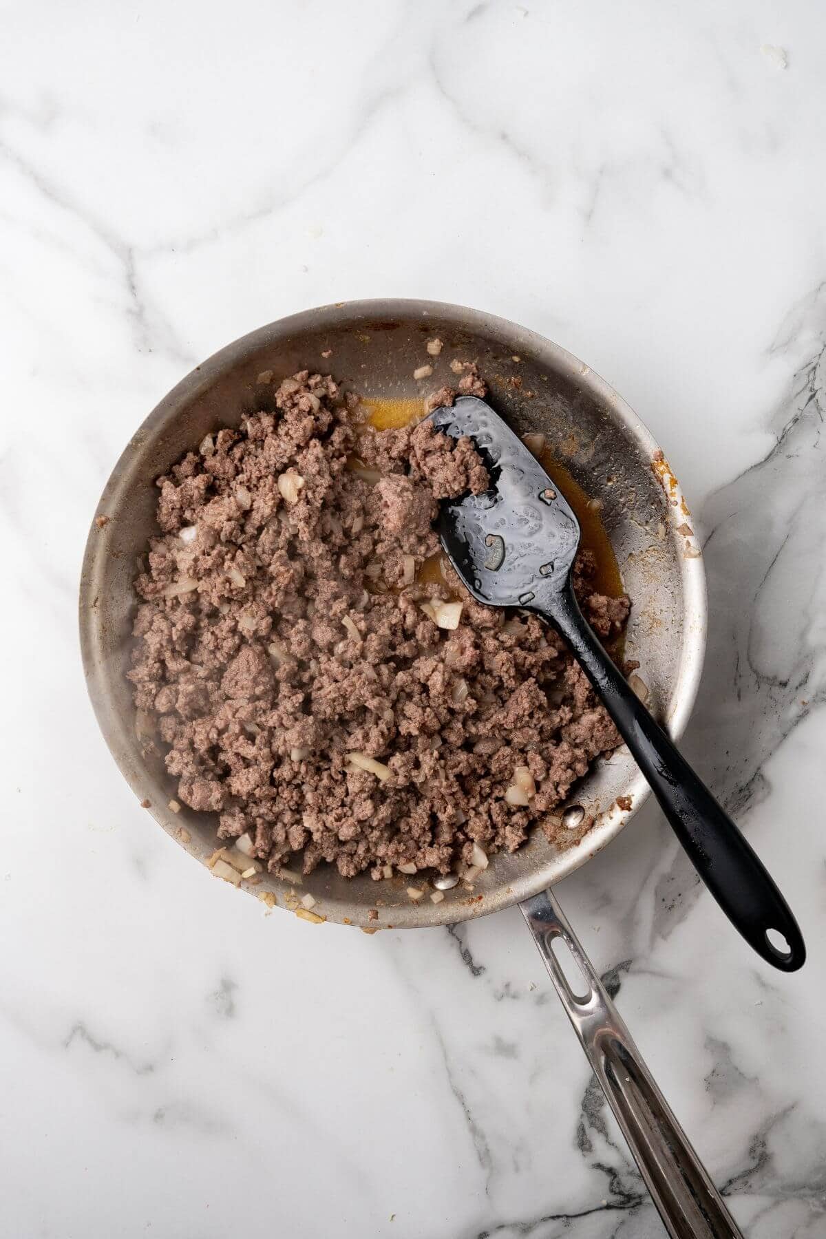 Ground beef and onions sizzle in a skillet, reminiscent of juicy Big Mac flavors, with a black spatula resting nearby on the marble countertop.