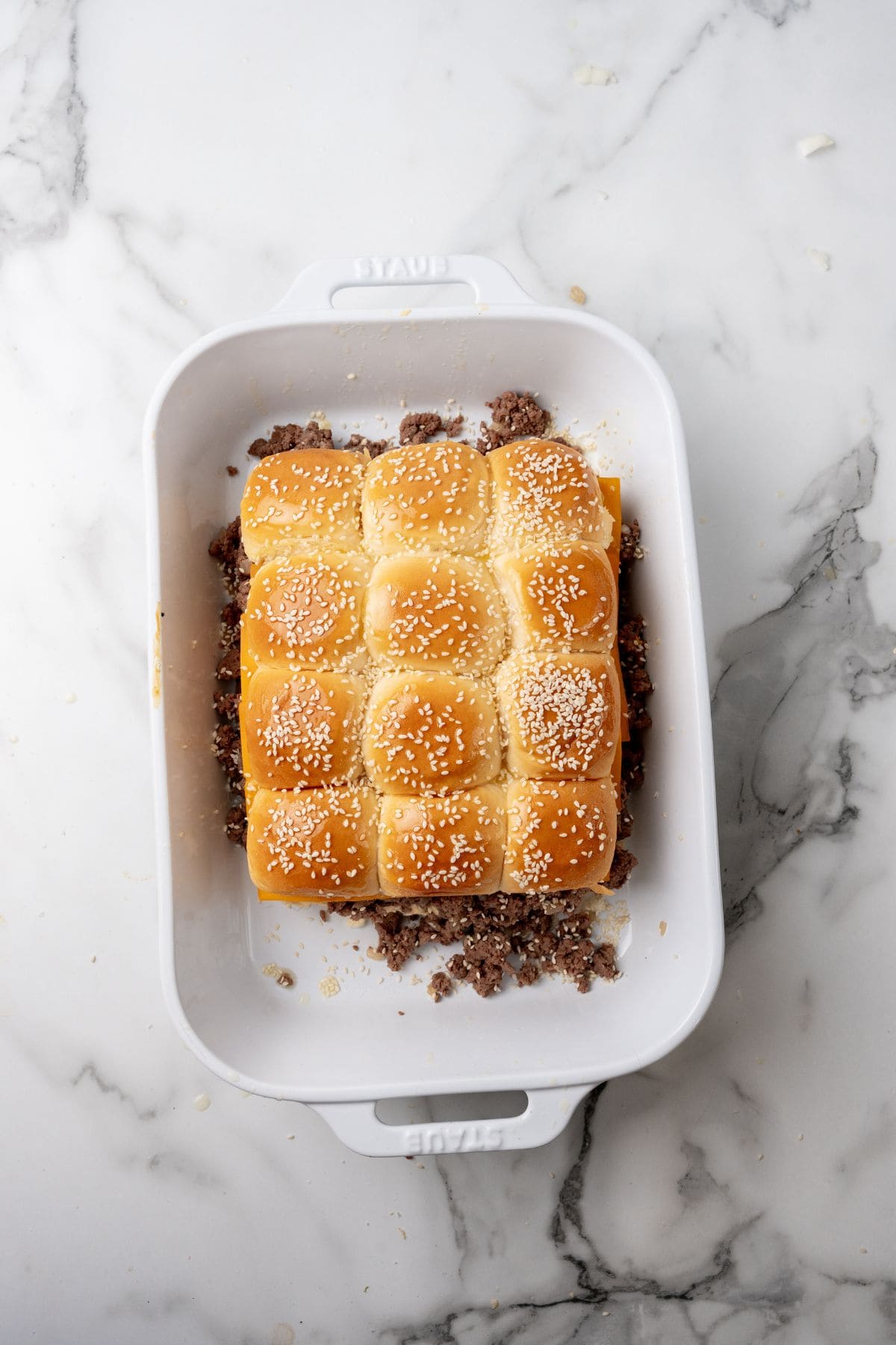 A tray of Big Mac Sliders with sesame seed buns and ground beef filling, arranged in a white baking dish on a marble surface.