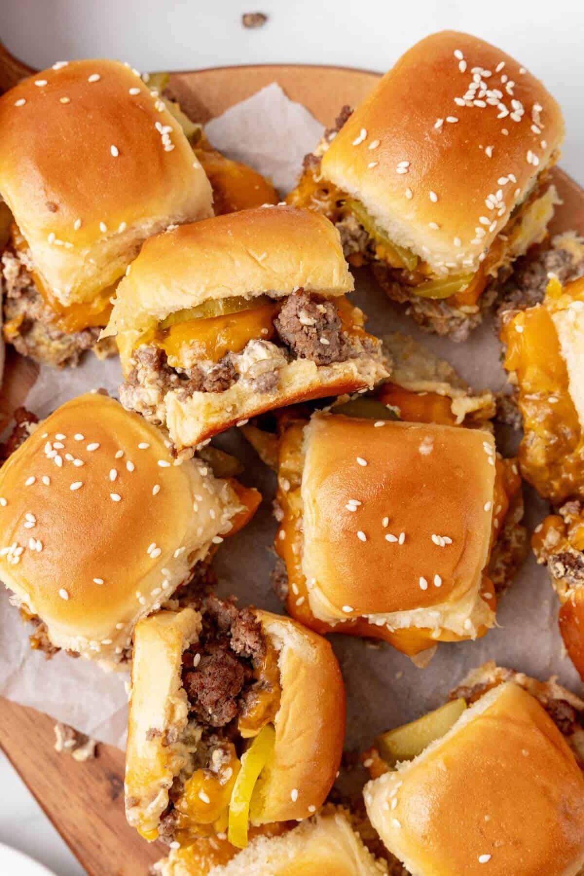 A mouthwatering array of Big Mac sliders featuring sesame seed buns, juicy beef patties, melted cheese, and tangy pickles arranged on a wooden board lined with parchment paper.