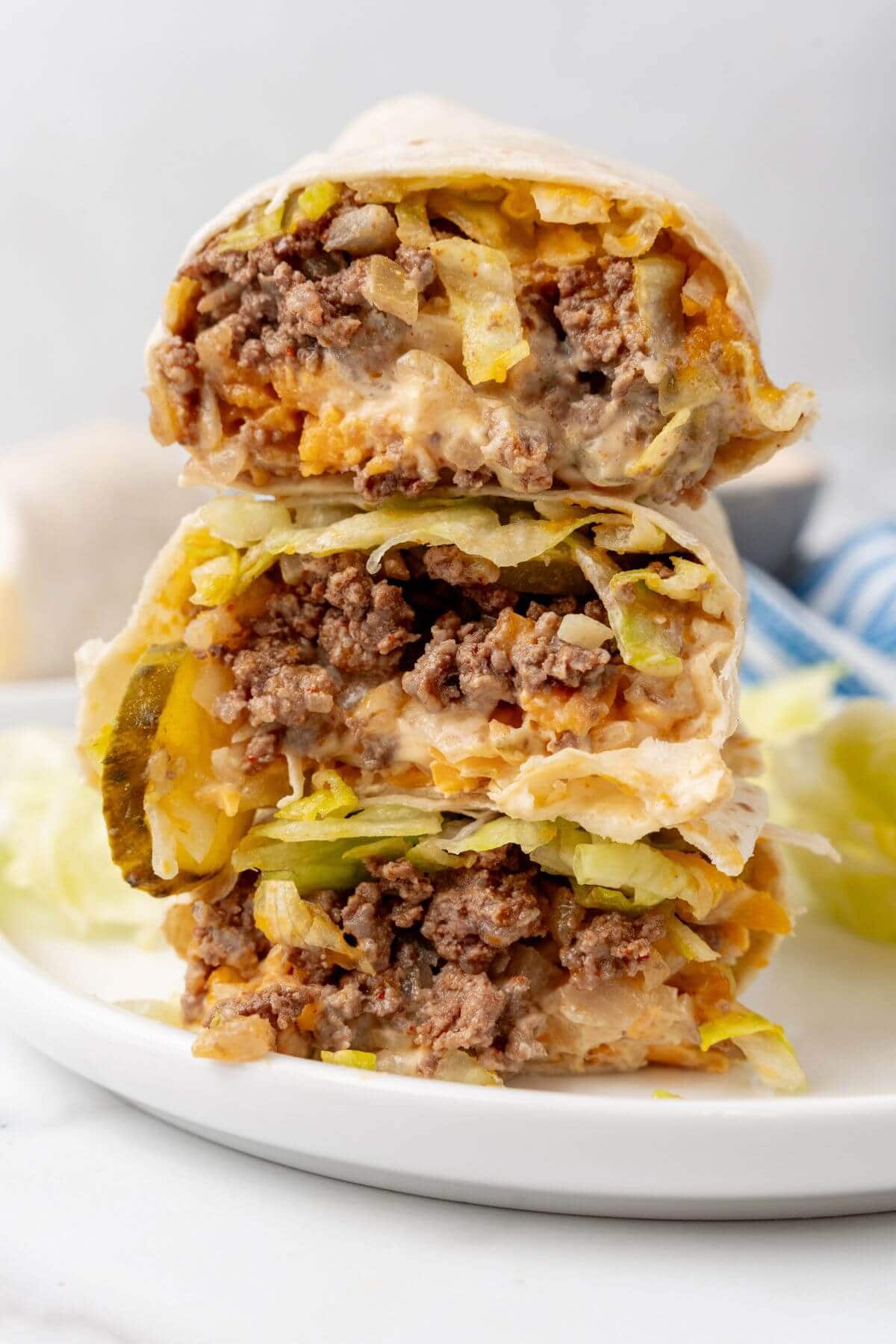 Three beef burrito halves, reminiscent of Big Mac flavors, are stacked on a white plate. They're filled with ground beef, crisp lettuce, melty cheese, and tangy sauce for a satisfying twist.