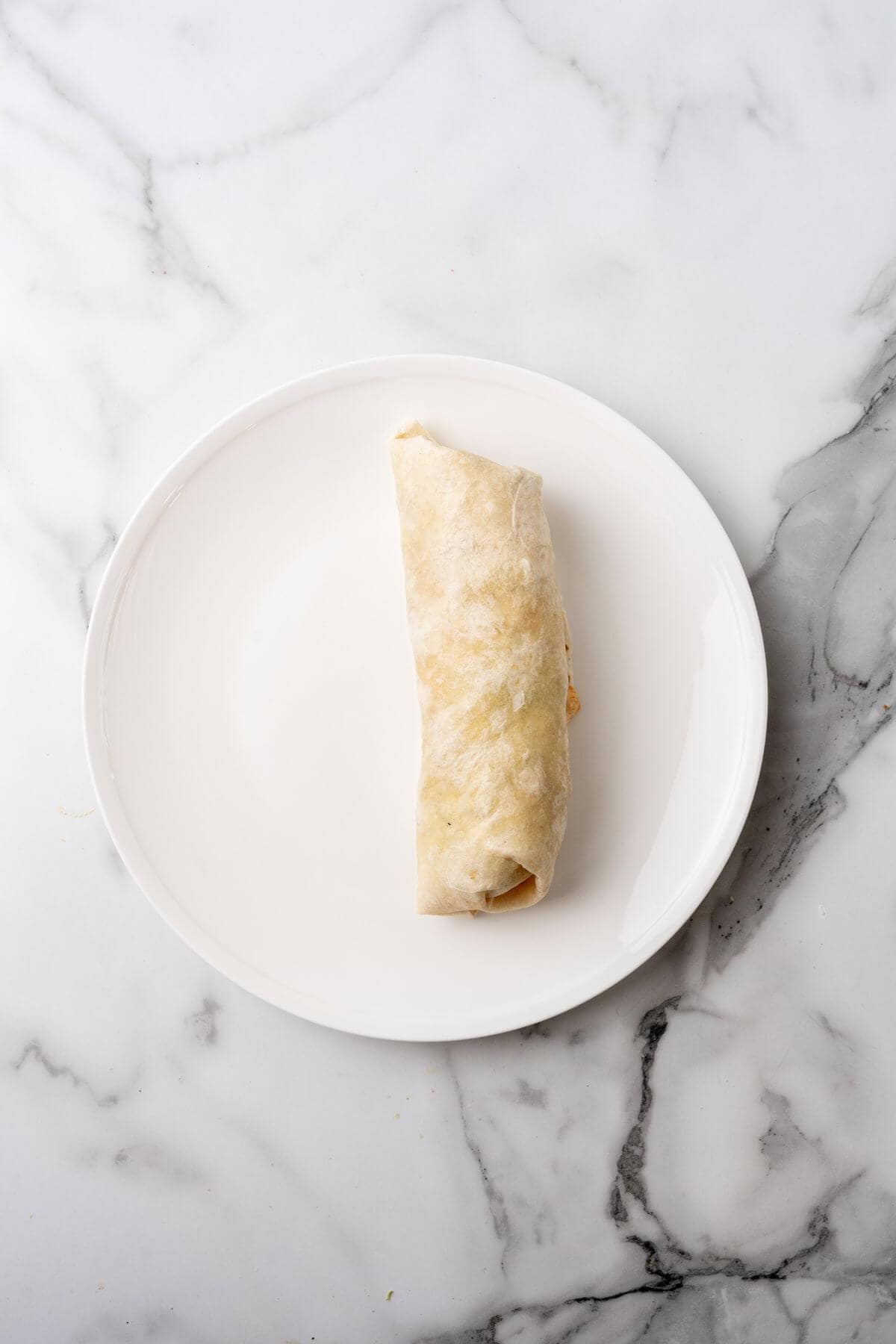 A single Big Mac Wrap rests elegantly on a white plate against a sleek marble background.