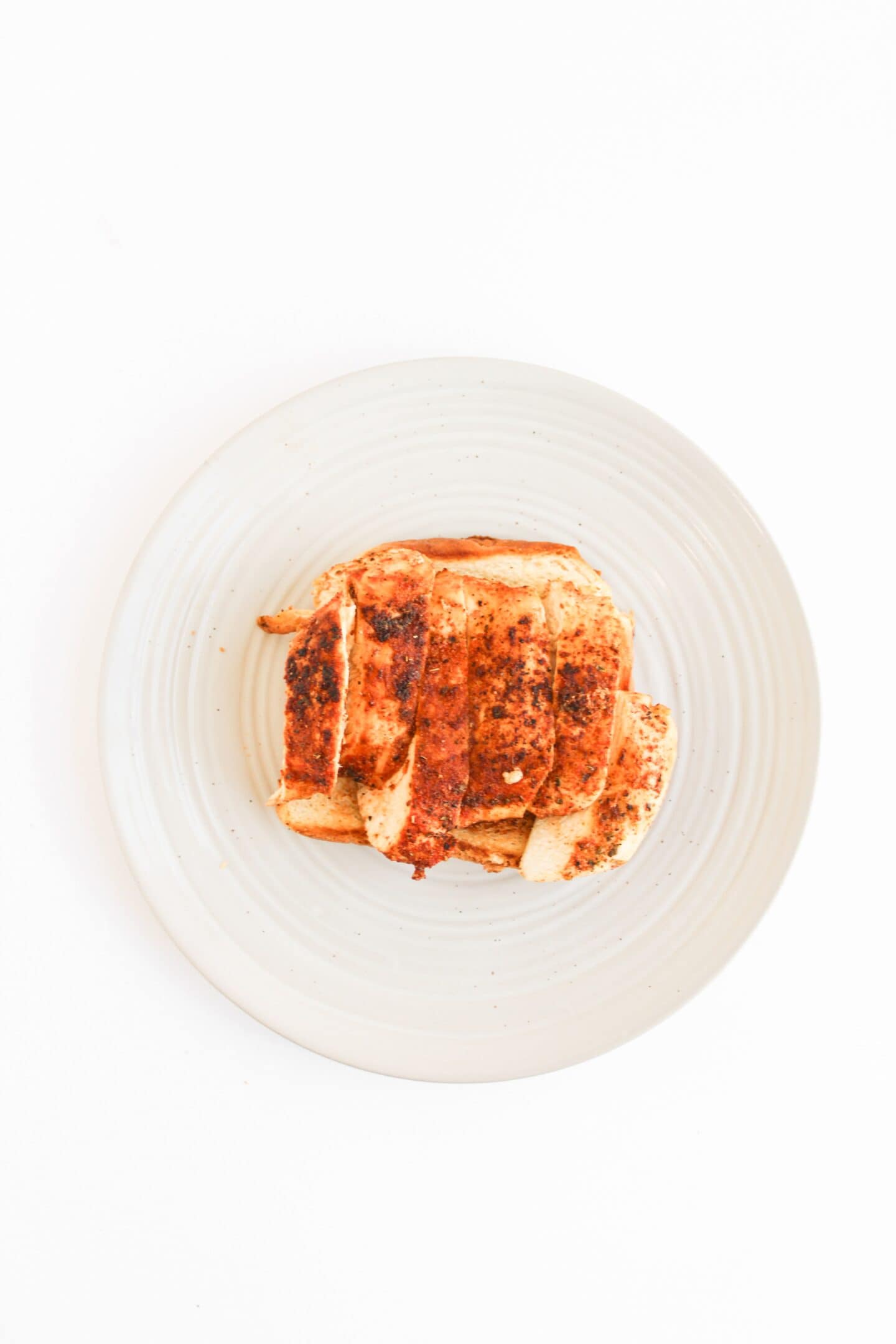 A plate with sliced, cooked, seasoned chicken breast—perfect for Blackened Chicken Clubs—on a white background.