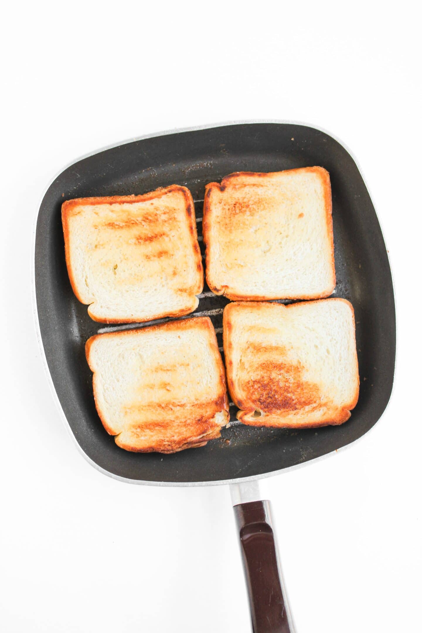 Four slices of toasted bread are arranged in a square inside a black frying pan with a handle, viewed from above on a white background—perfect for building your own Blackened Chicken Club or classic Chicken Clubs.