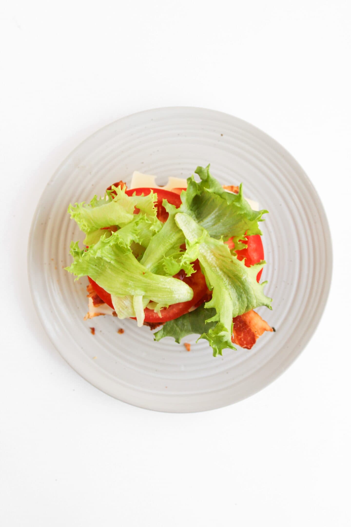 Open-faced Blackened Chicken Club sandwich with lettuce, tomato, and cheese on a plate, photographed from above against a white background.