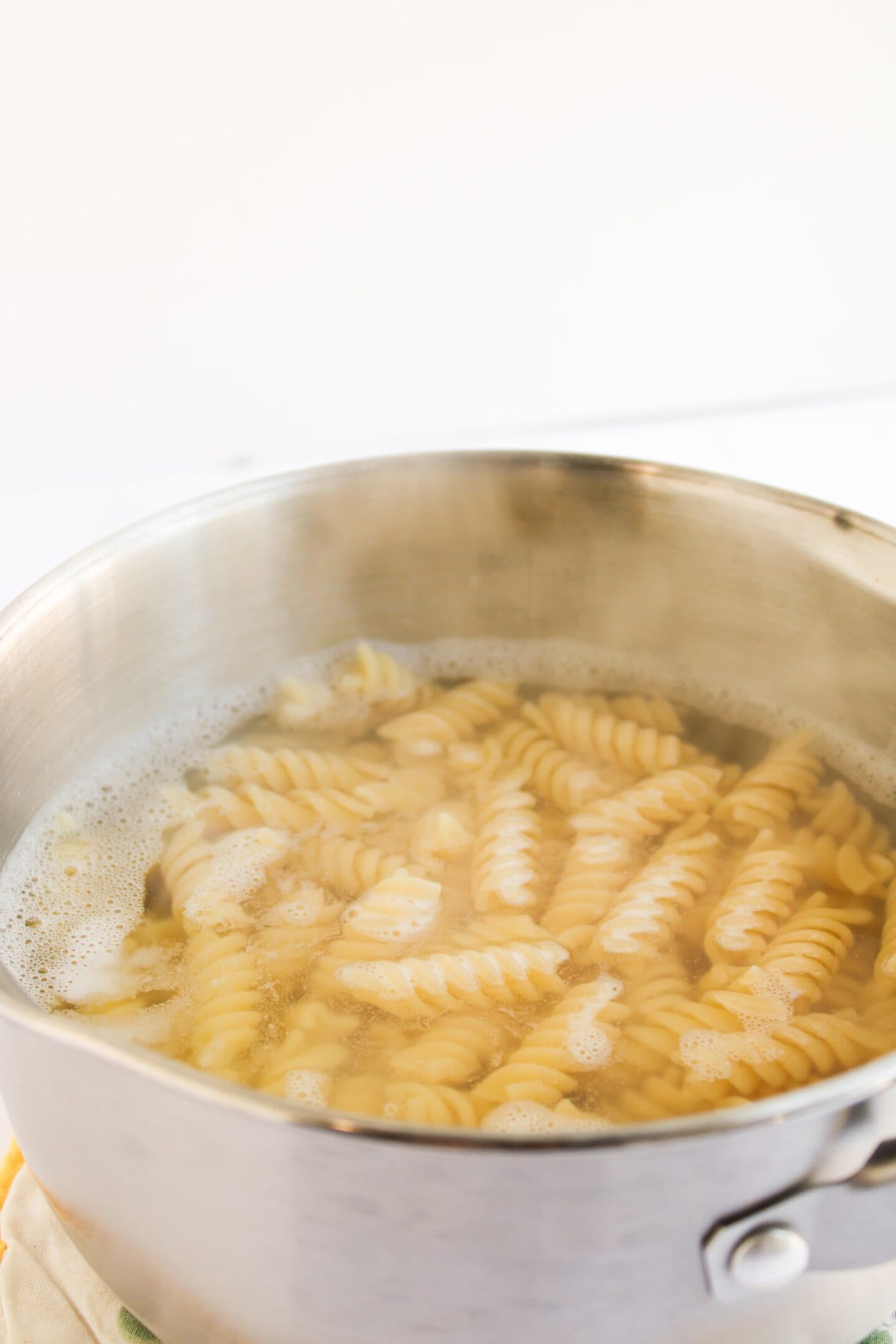 A stainless steel pot filled with boiling water and rotini pasta cooking on a stove, perfect for preparing a delicious Chicken Caesar Pasta Salad.
