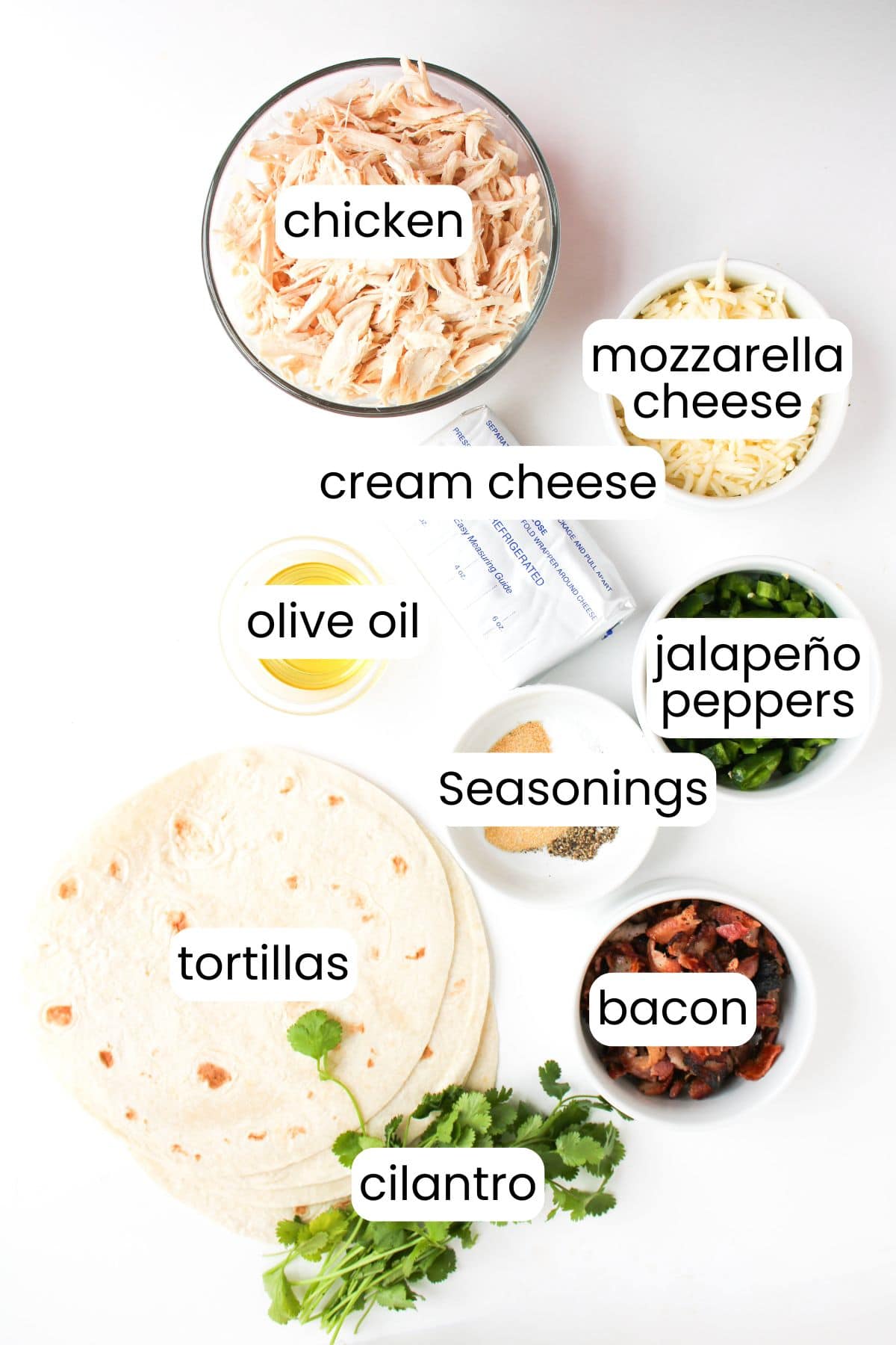 Ingredients for Jalapeño Popper Chicken: shredded chicken, mozzarella cheese, cream cheese, olive oil, jalapeño peppers, seasonings, tortillas, bacon, and cilantro neatly arranged on a white surface.