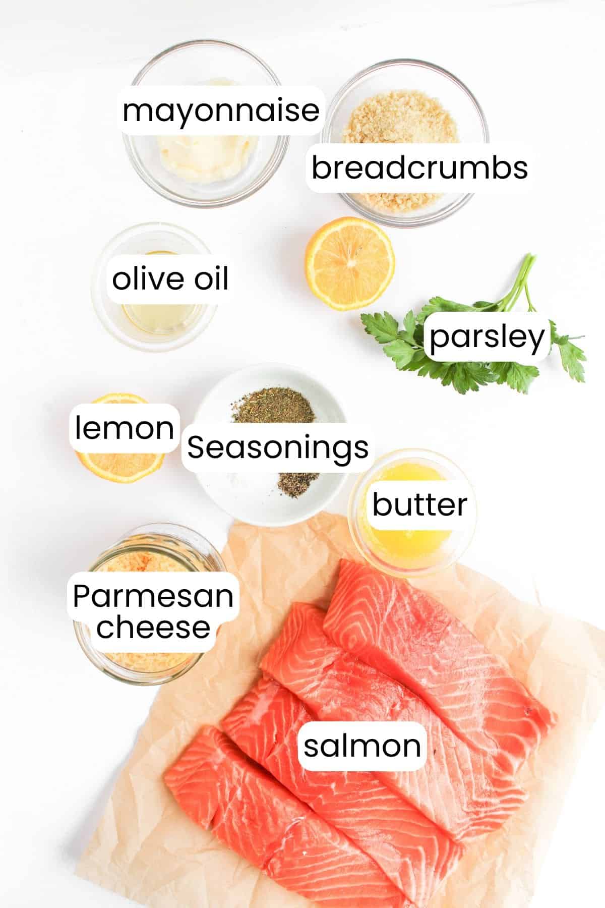 A delectable salmon recipe featuring panko-crusted fillets. Ingredients include salmon, mayonnaise, breadcrumbs, olive oil, lemon, parsley, seasonings, butter, and Parmesan cheese—all artfully arranged on a pristine white surface.