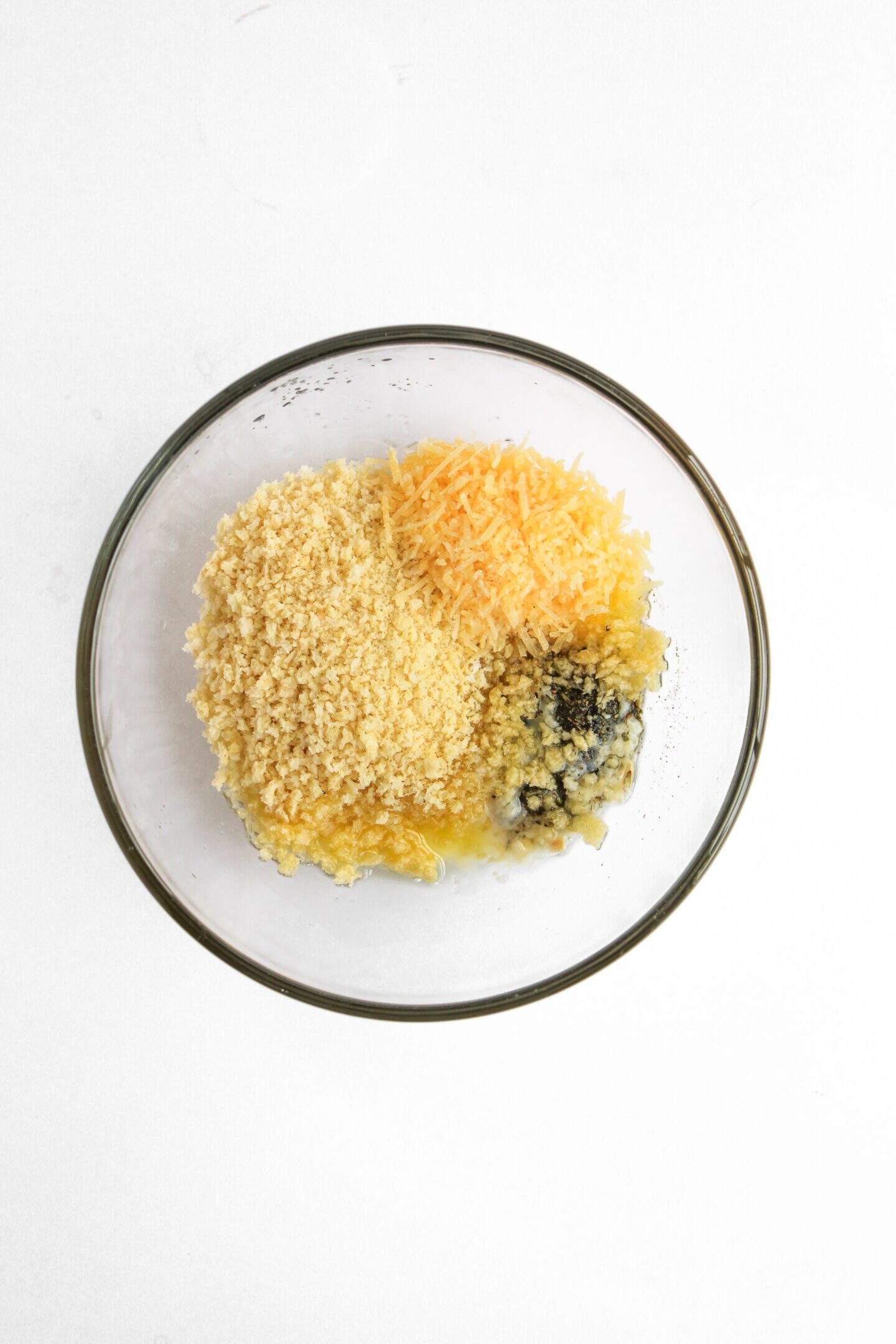 A glass bowl brimming with ingredients: breadcrumbs, shredded cheese, minced garlic, and a seasoning blend awaits your culinary touch. Perfect for crafting a delectable panko-crusted creation or enhancing the flavors of baked salmon.