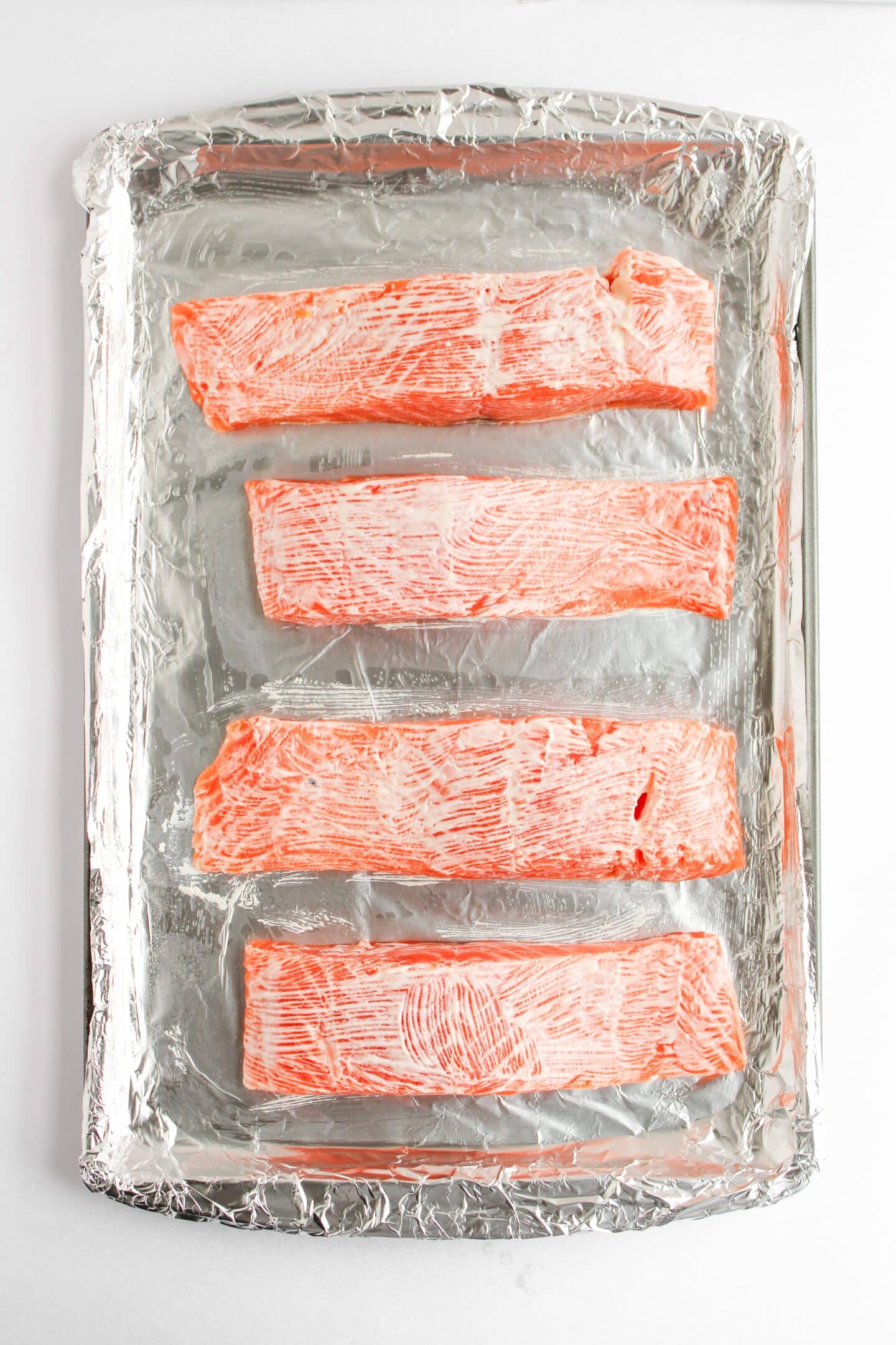 Four raw salmon fillets, soon to be a delightful baked salmon dish, rest on a foil-lined baking sheet, waiting to be transformed into a succulent Panko-crusted masterpiece.
