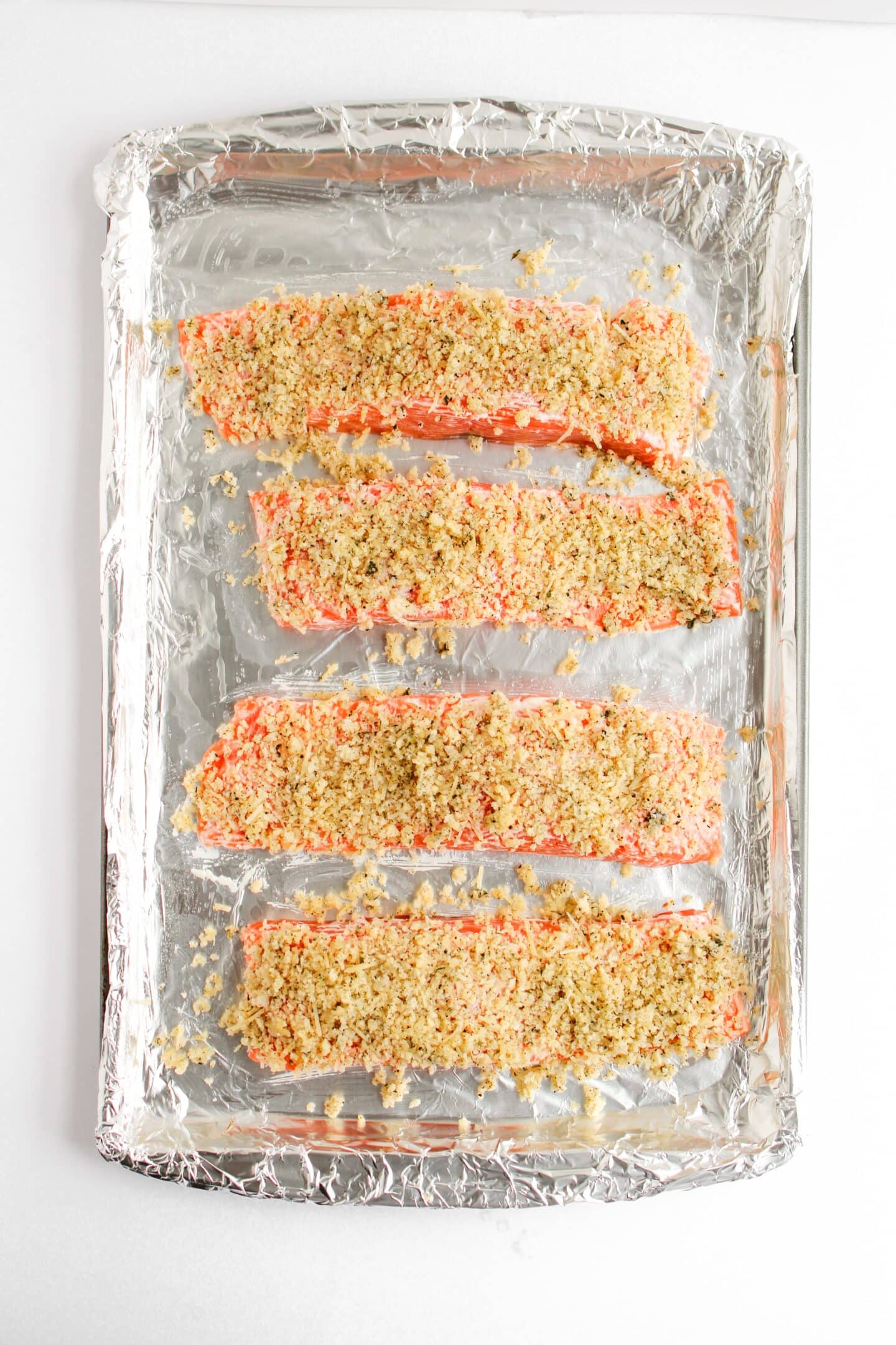 Four panko-crusted salmon fillets rest on a foil-lined baking sheet, perfect for a delicious baked salmon recipe.