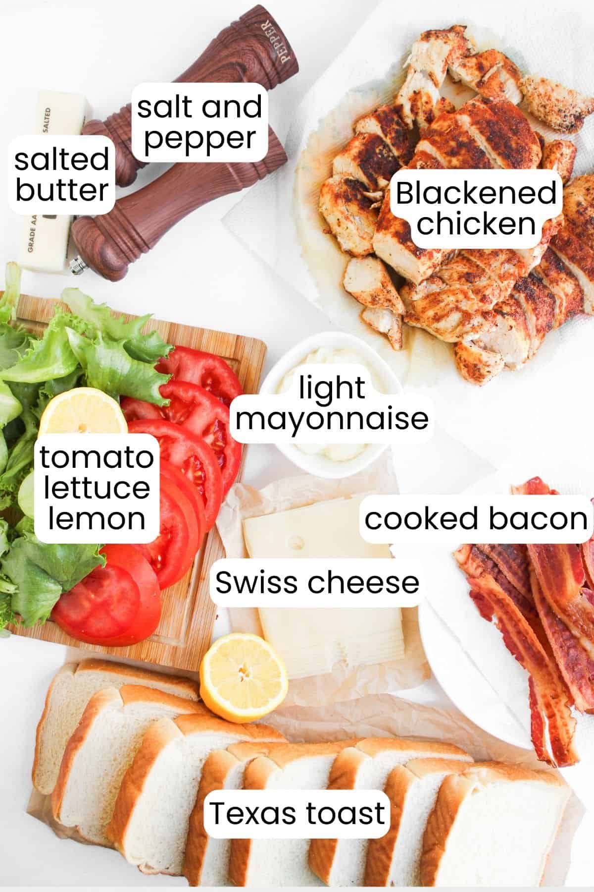 Ingredients for a Blackened Chicken Club are arranged on a table, including Texas toast, Swiss cheese, cooked bacon, blackened chicken, lettuce, tomato, lemon, light mayonnaise, butter, and seasonings.