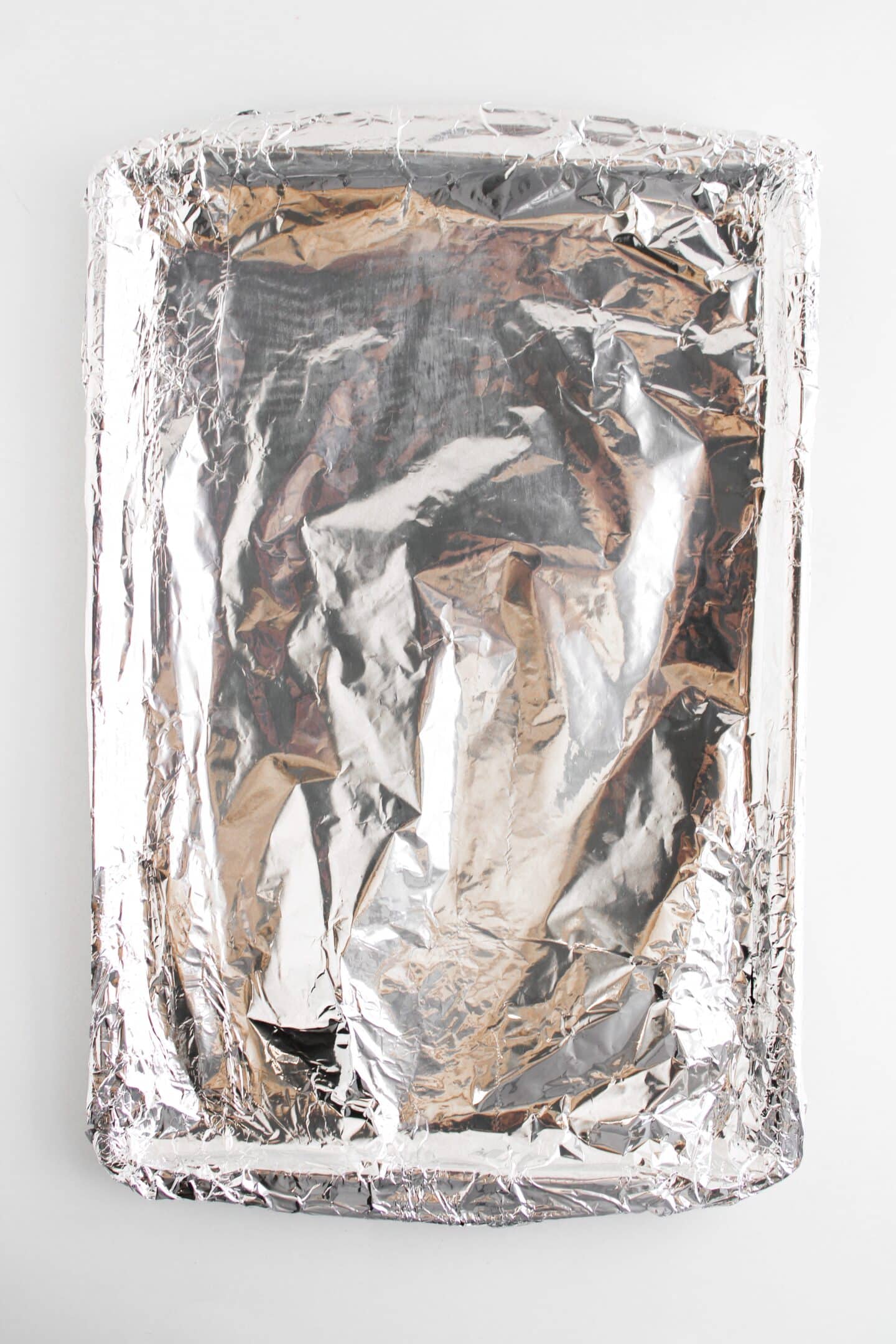 A sheet pan covered with aluminum foil rests on a white background, ready to roast veggies or bake mini meatloaf delights.