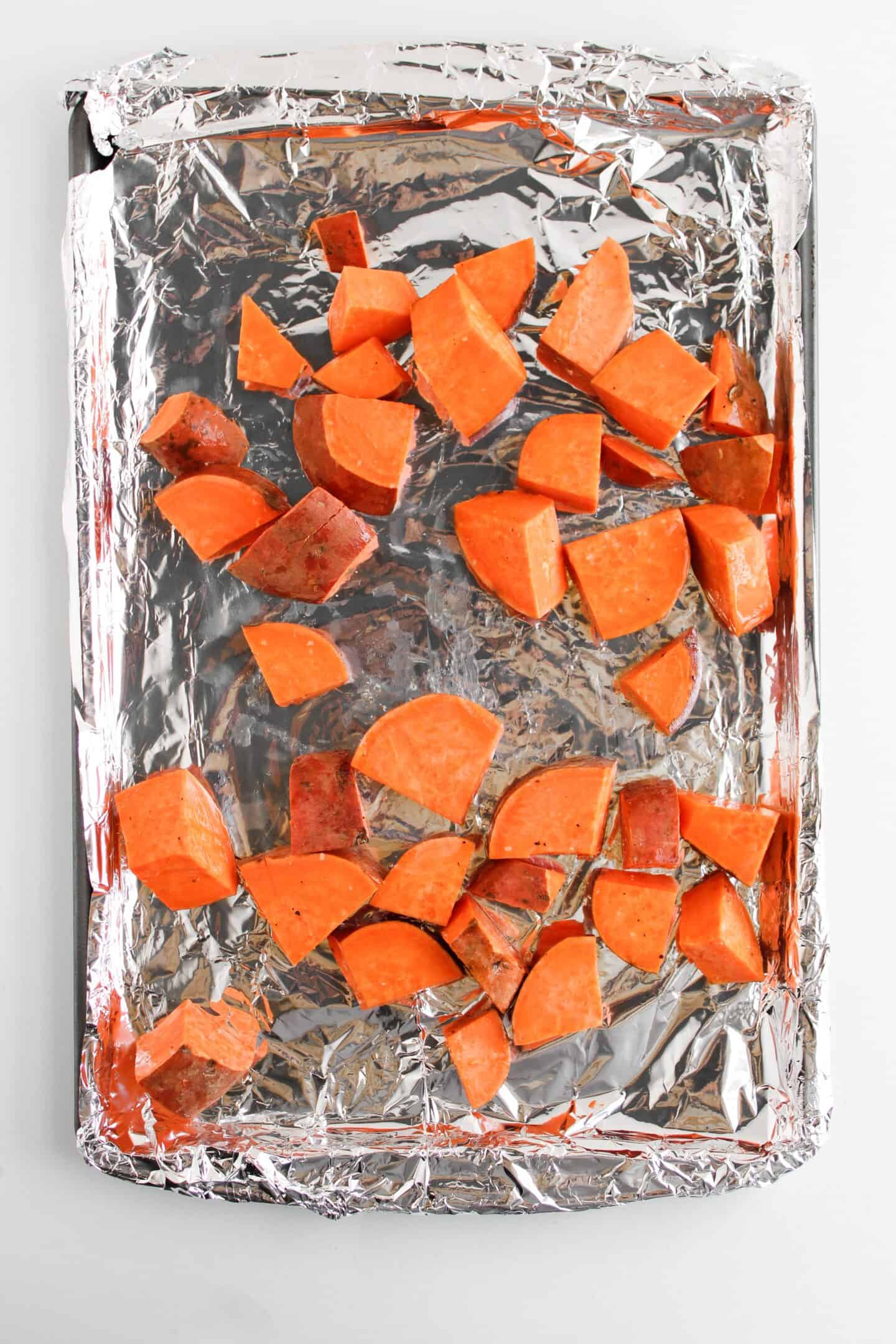 Chopped sweet potatoes on a foil-lined sheet pan, ready for roasting alongside mini meatloaf for a delightful dinner.