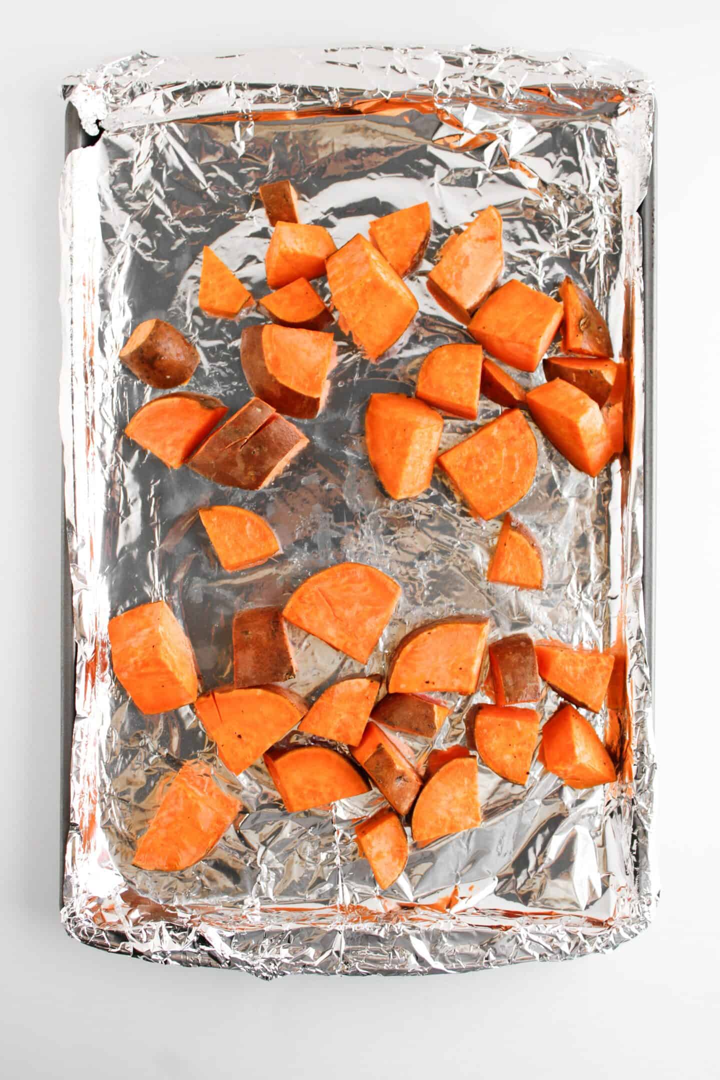 Chopped sweet potatoes cozy up with vibrant veggies on a foil-lined sheet pan, creating a colorful medley ready for roasting alongside mini meatloaf delights.